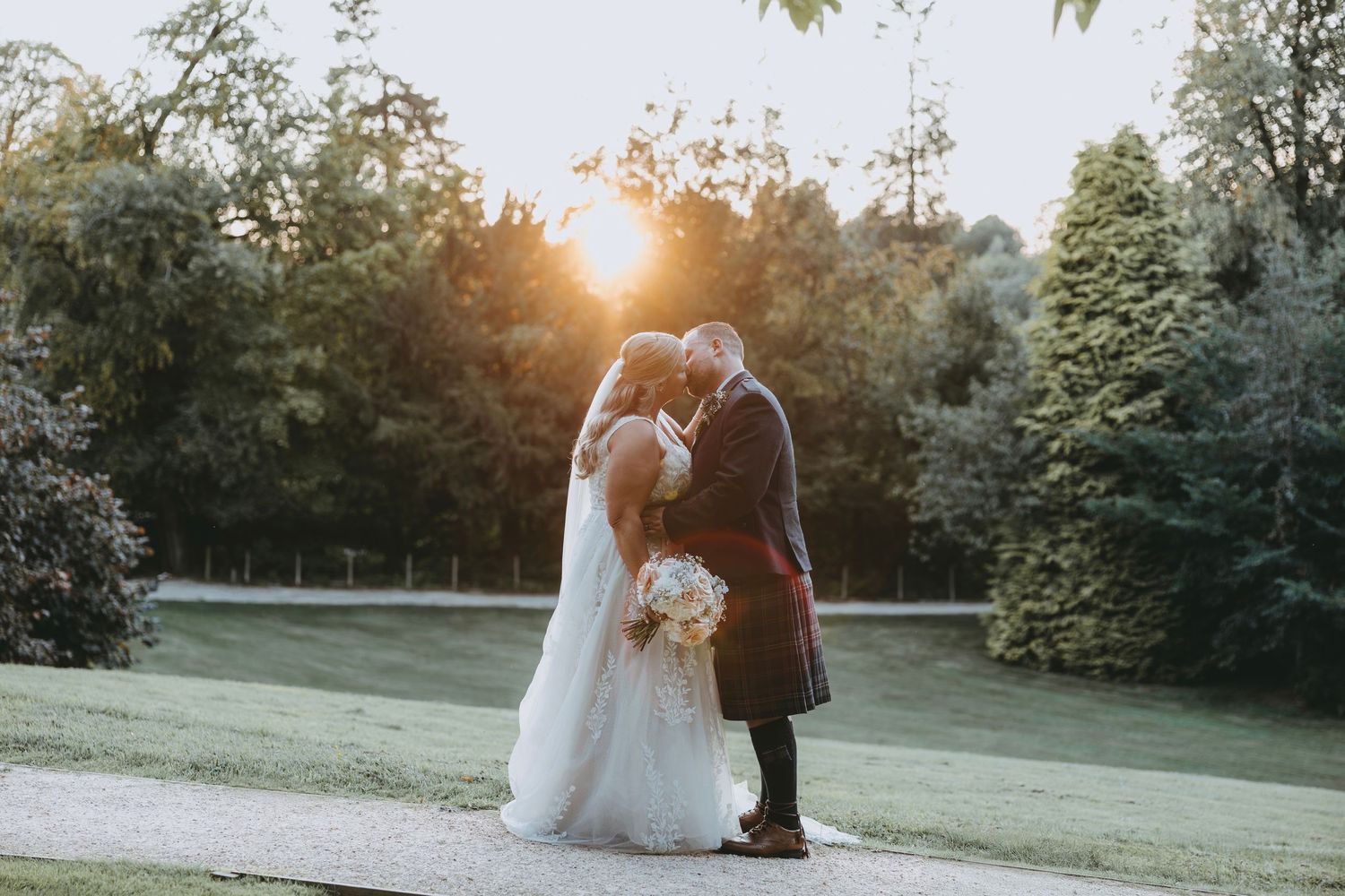 A romantic wedding photoshoot at sunset in a lush garden setting with golden light filtering through the trees.