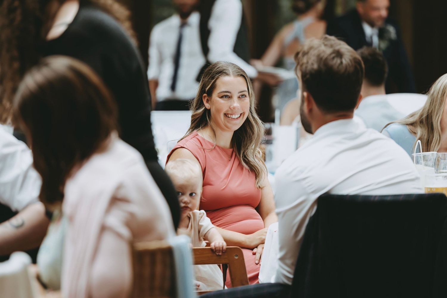 Guests mingling and socializing at a formal event with natural lighting streaming through windows.