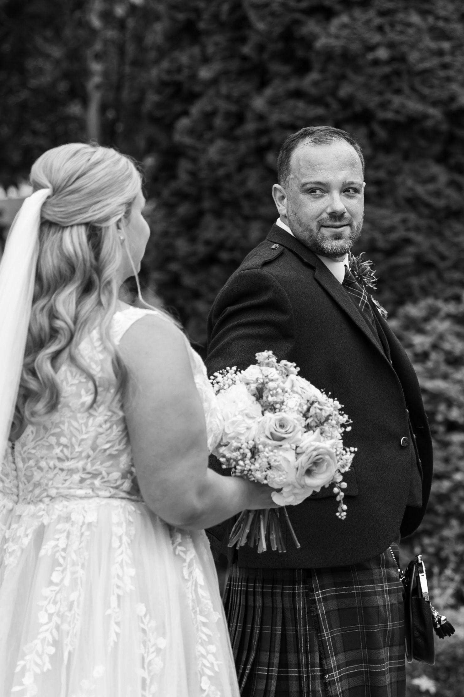 Wedding couple in traditional Scottish attire sharing an intimate moment with white bouquet.