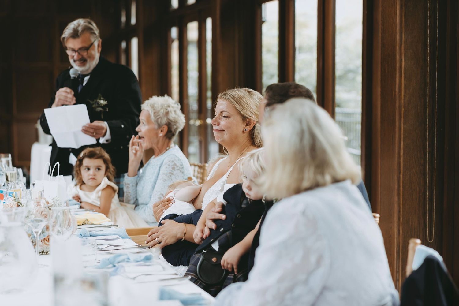 Wedding guests seated at elegant tables in a rustic wooden venue during reception celebration.