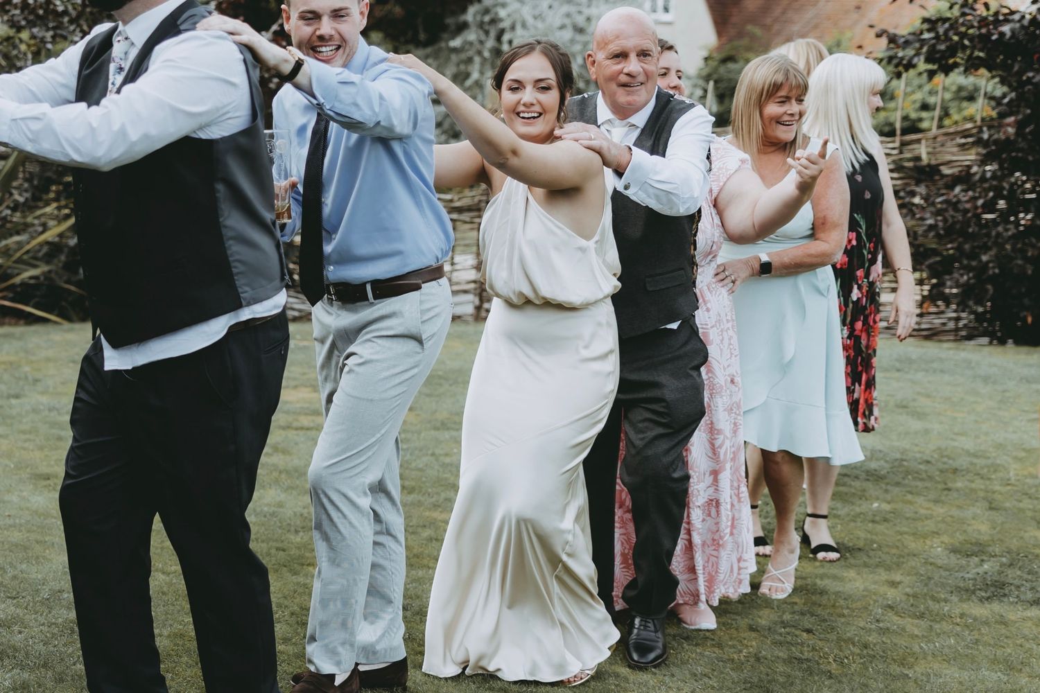 Joyful wedding celebration with guests dancing in a garden setting.