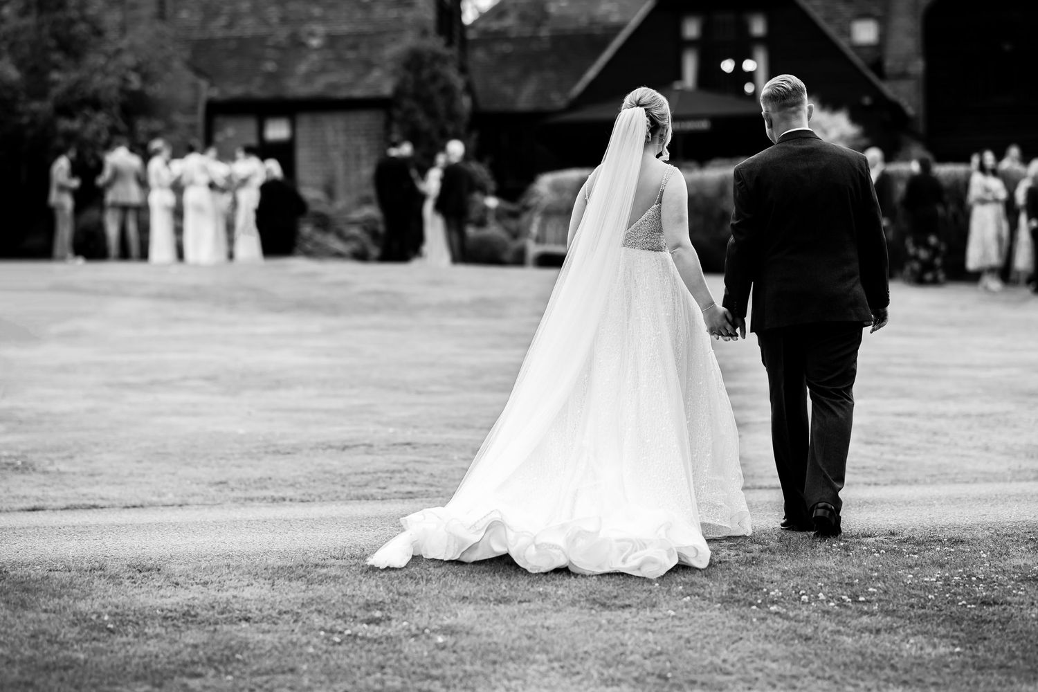 Black and white photo of a bride and groom walking together outdoors during their wedding ceremony.