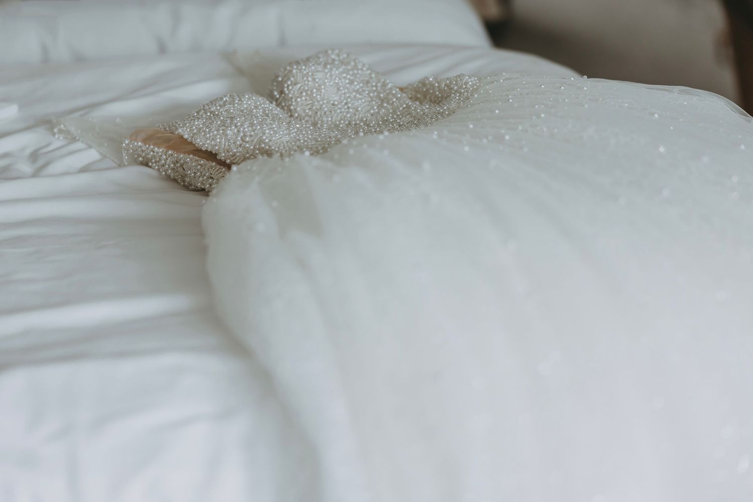 White wedding dress fabric laid out on soft bedding showing elegant details.
