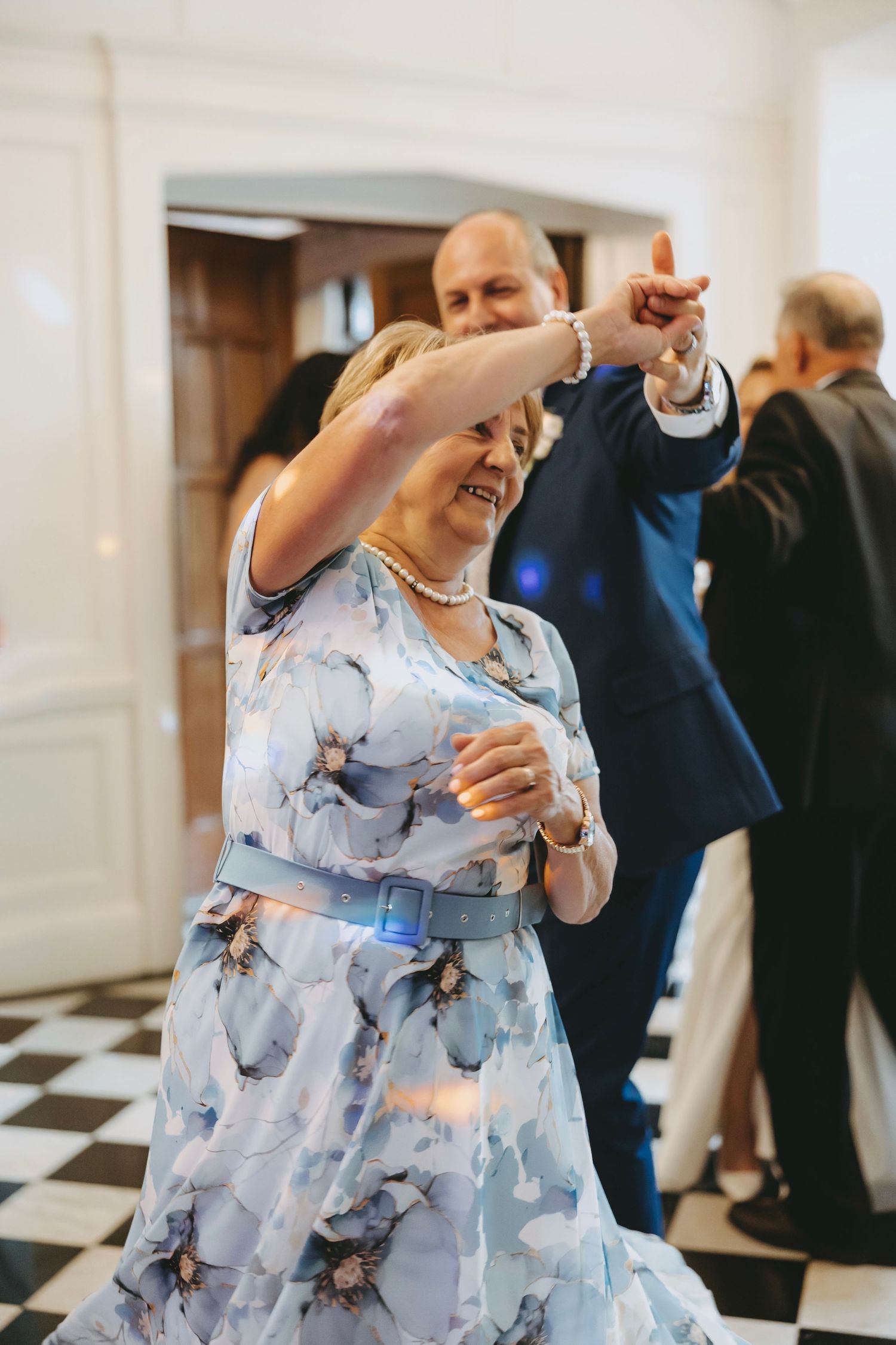 Woman in light blue floral dress twirling while dancing on checkered floor.