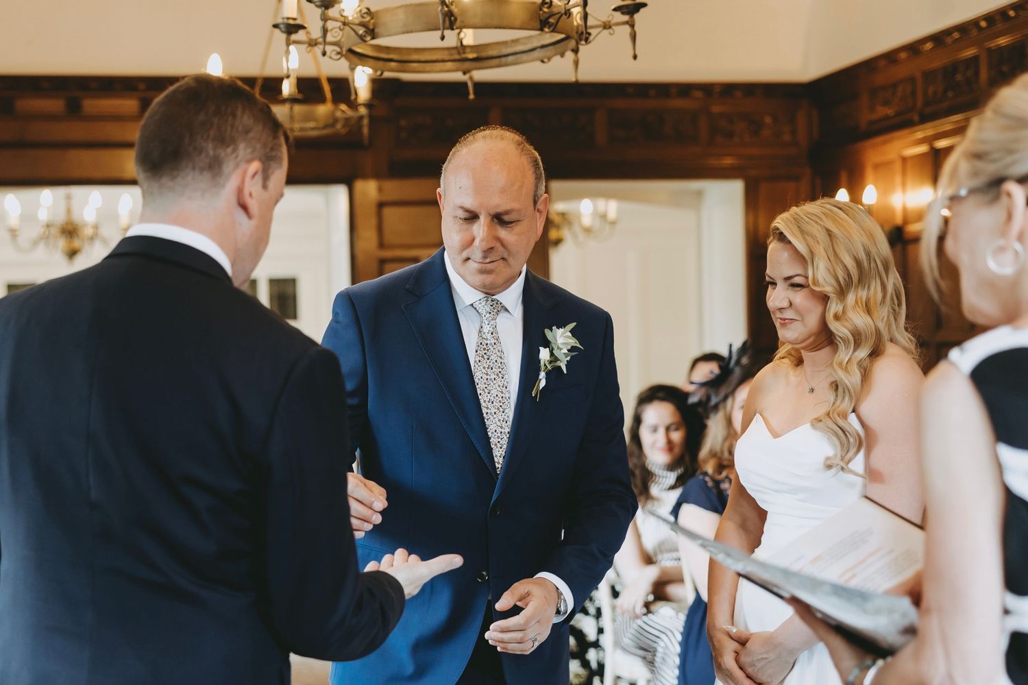 Wedding ceremony participants gather in an elegant venue with traditional decor and lighting.