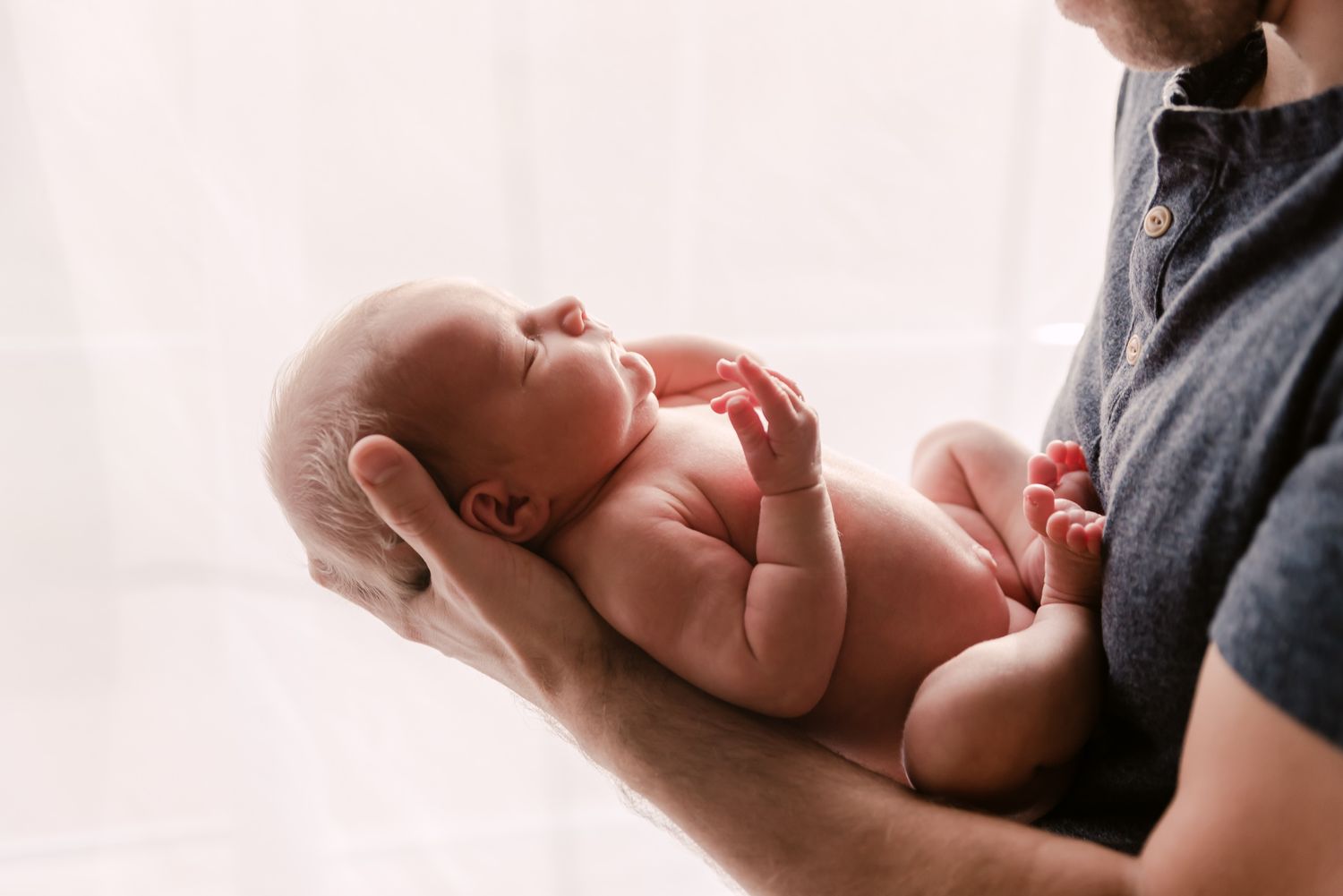 Gentle hands cradle a sleeping newborn baby against soft fabric.