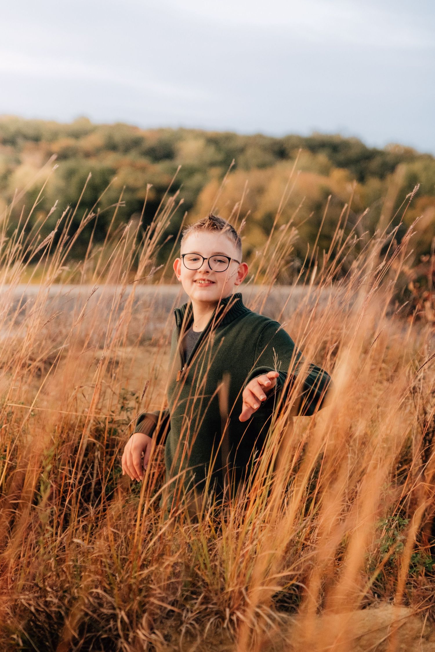 Person sitting among tall golden grass during sunset with water in background.