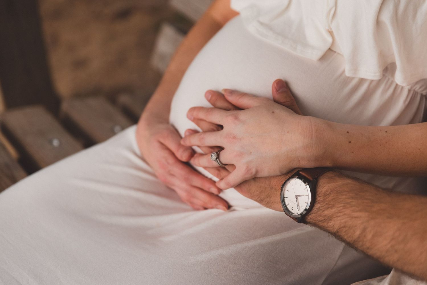 Tender moment of hands cradling a newborn baby wrapped in white.
