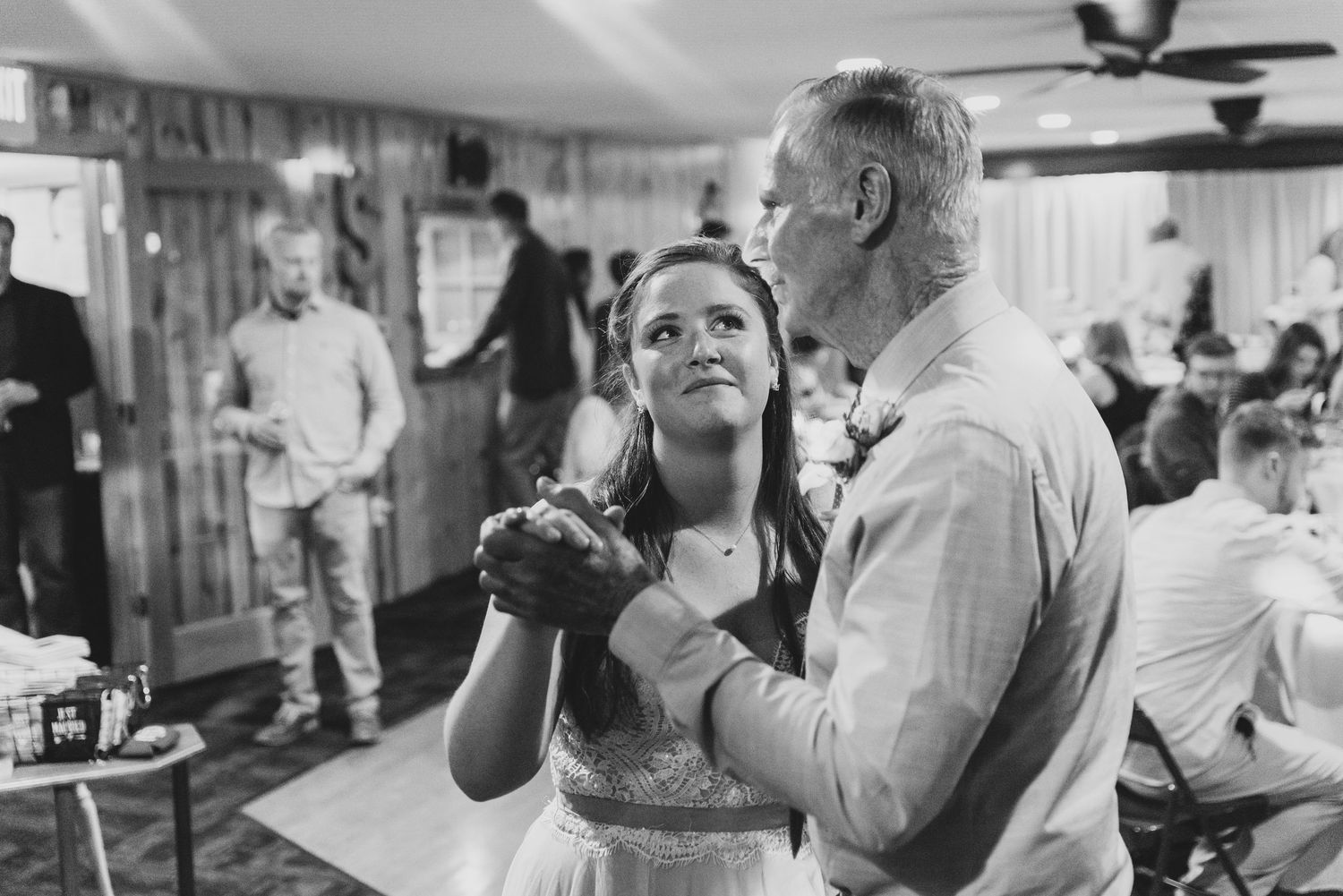 Black and white photo of wedding reception dancing with ceiling fans visible overhead.