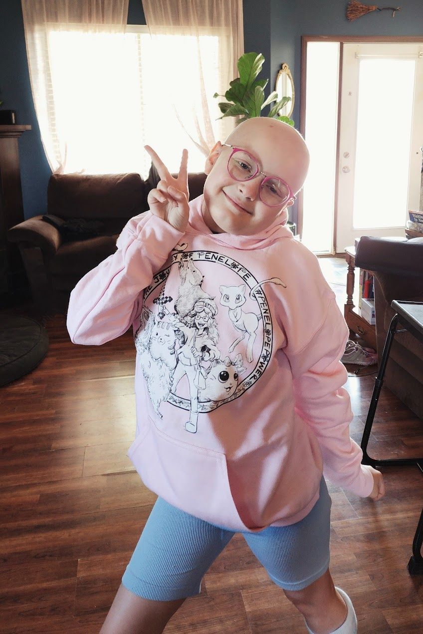 Person in pink sweatshirt and blue shorts posing playfully indoors.