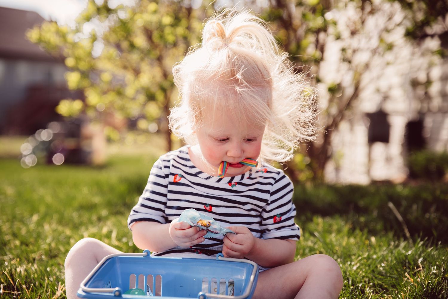Child sitting on grass reading a blue book outdoors on sunny day.