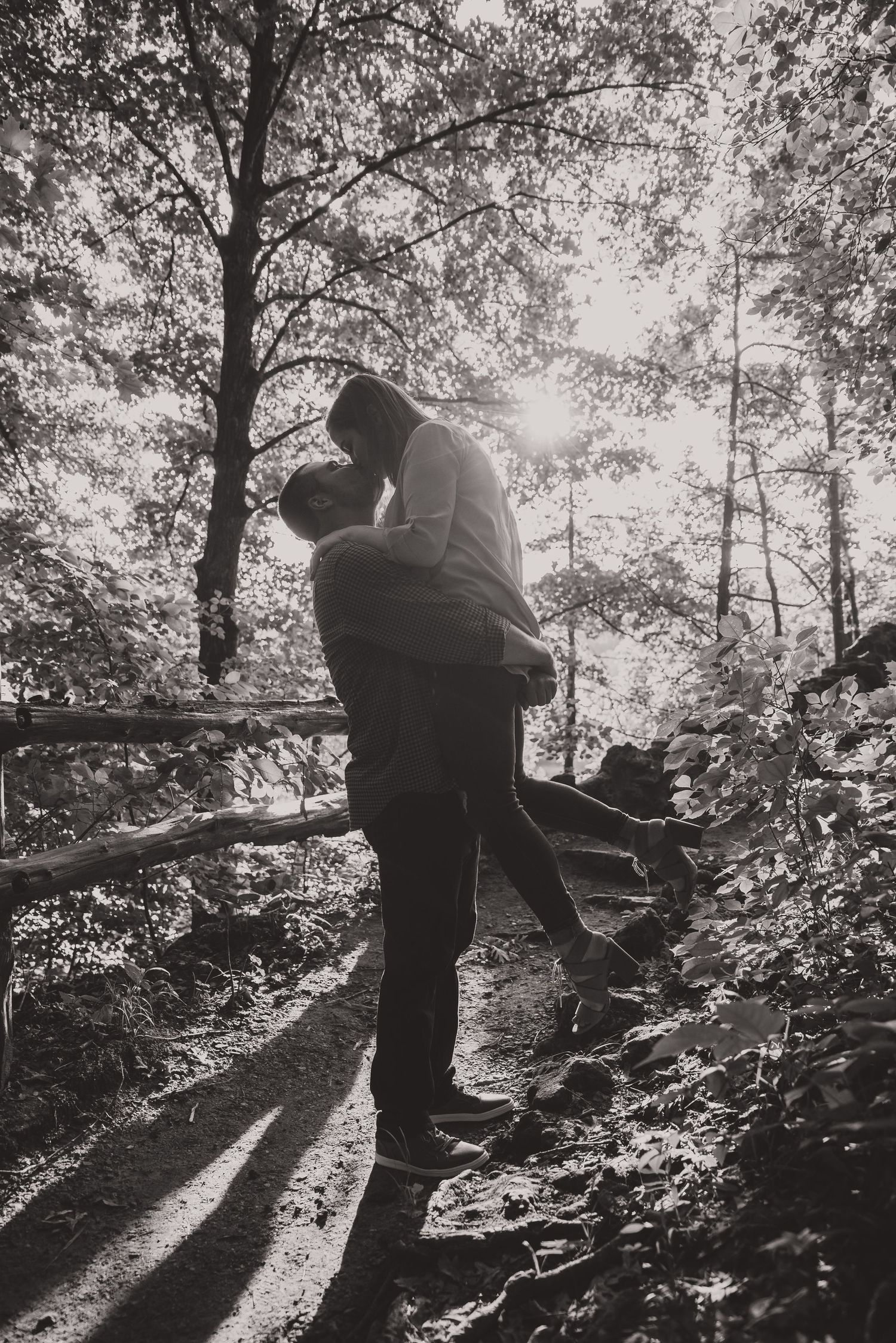 Artistic black and white silhouettes of a couple in a sunlit forest setting.