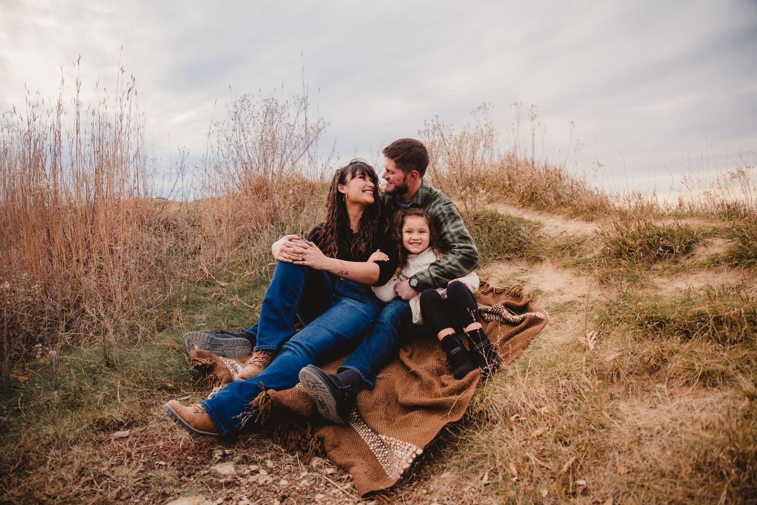 Family relaxing on a blanket with their dog in a field of tall grass.
