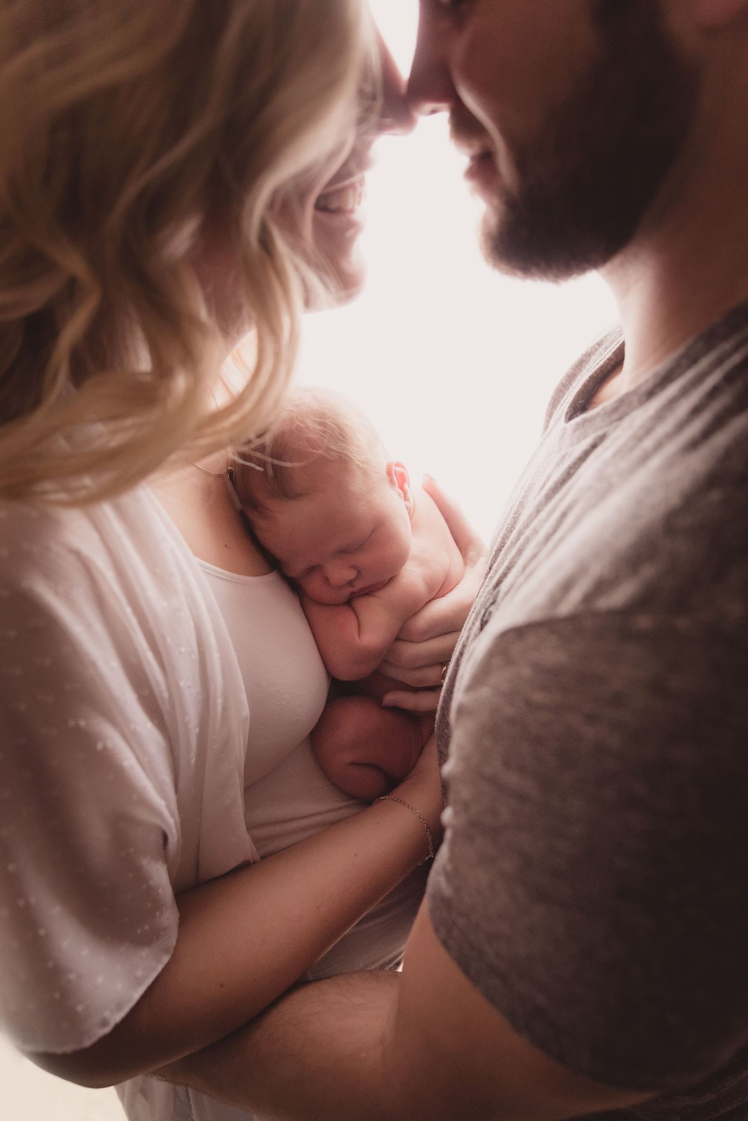 Intimate family moment with parents cradling their newborn baby in soft lighting.