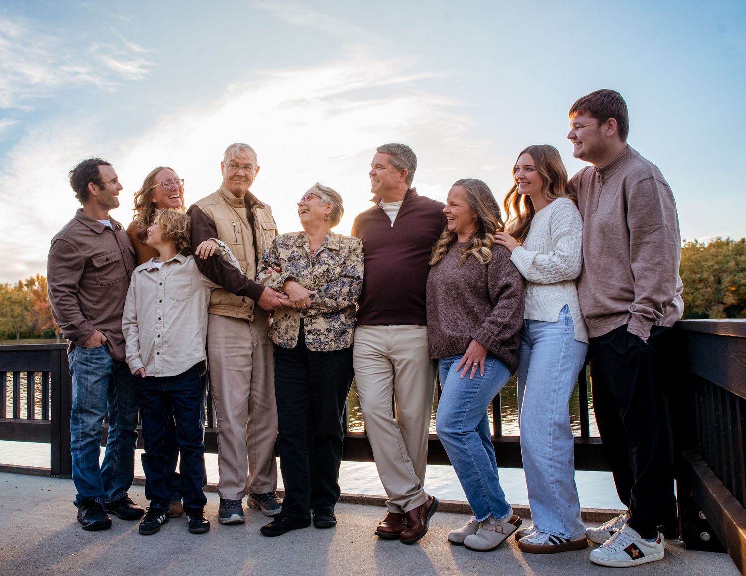 Group of people sitting casually on a railing during sunset by the water.