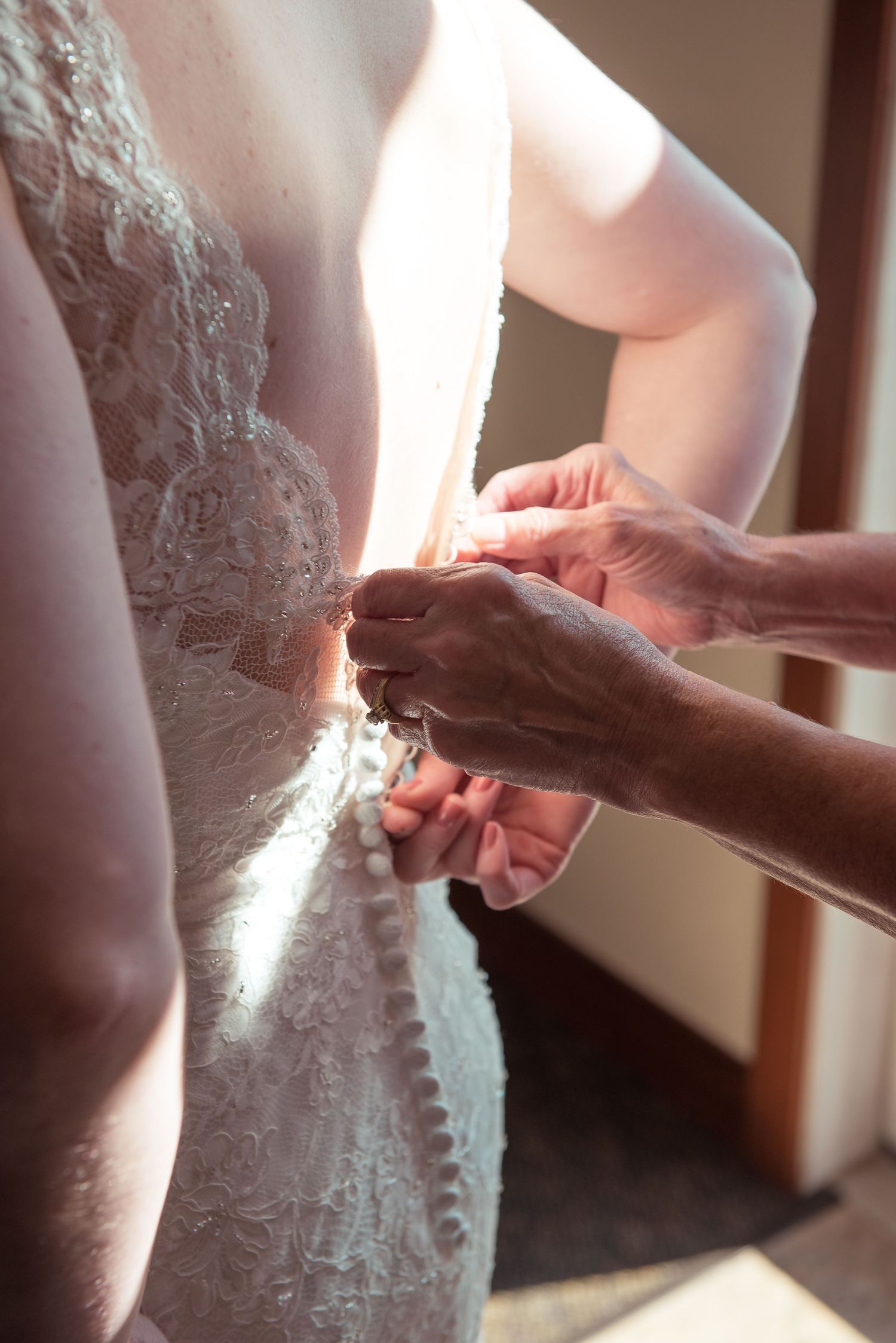 Close-up shots of hands adjusting the back of a white lace wedding dress.