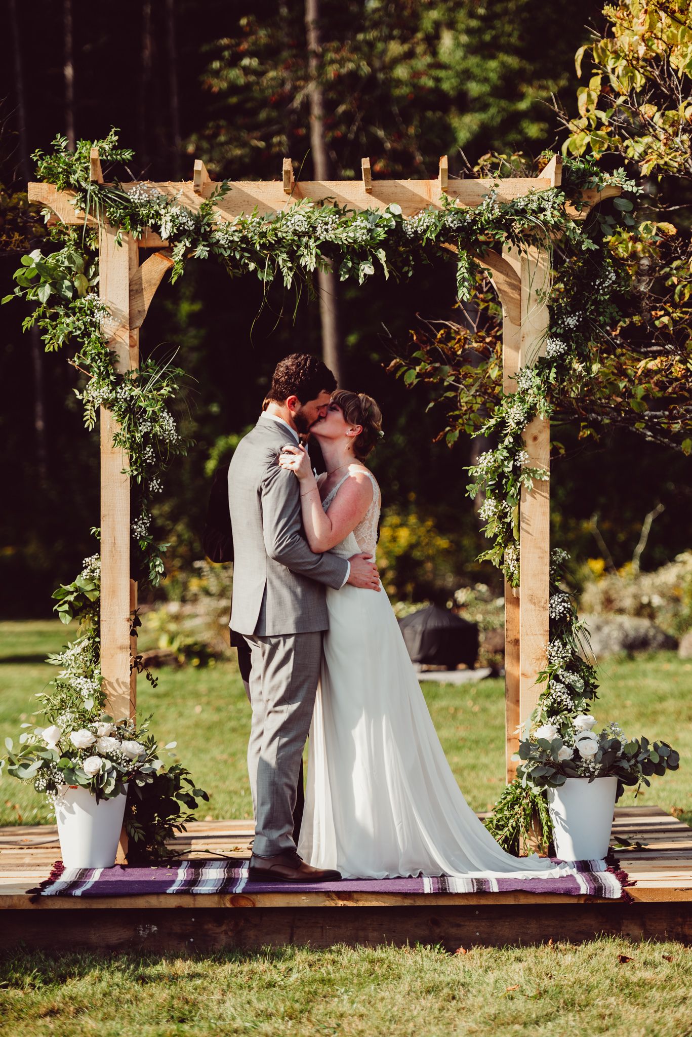 Couple sharing intimate moment under wooden arch decorated with greenery and flowers.