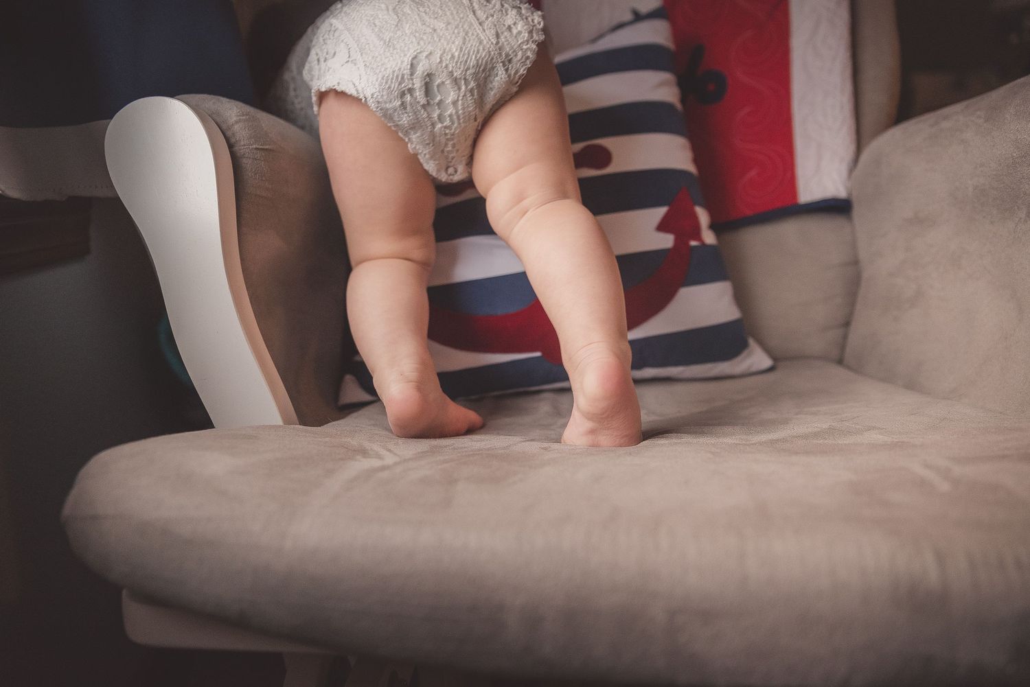 Small baby feet and legs exploring a grey couch cushion.
