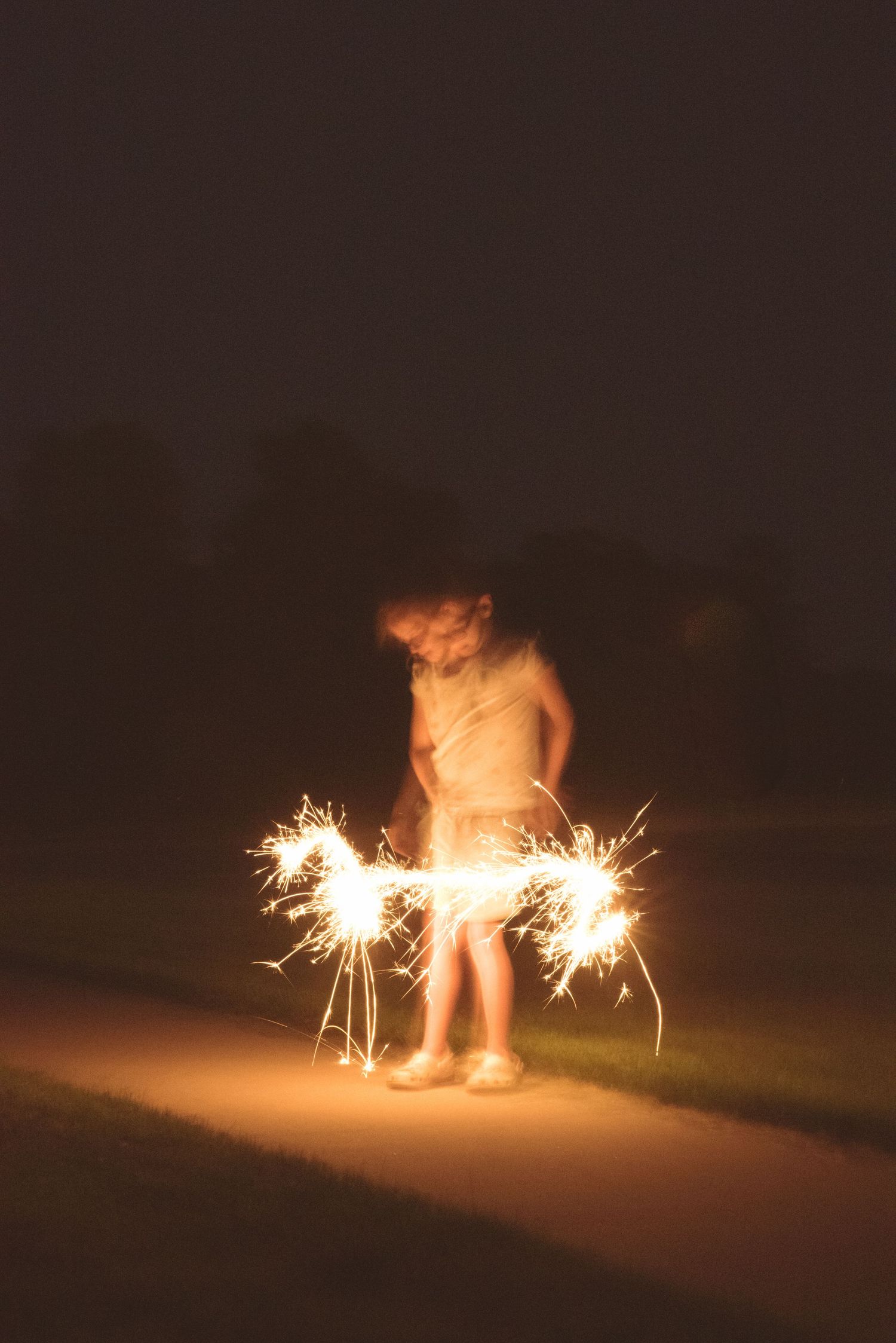 Person playing with sparklers at night creating glowing light patterns.