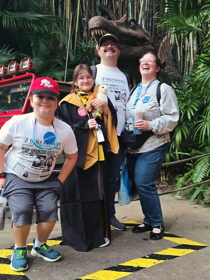 People standing in line at a theme park or attraction with tropical plants in background.