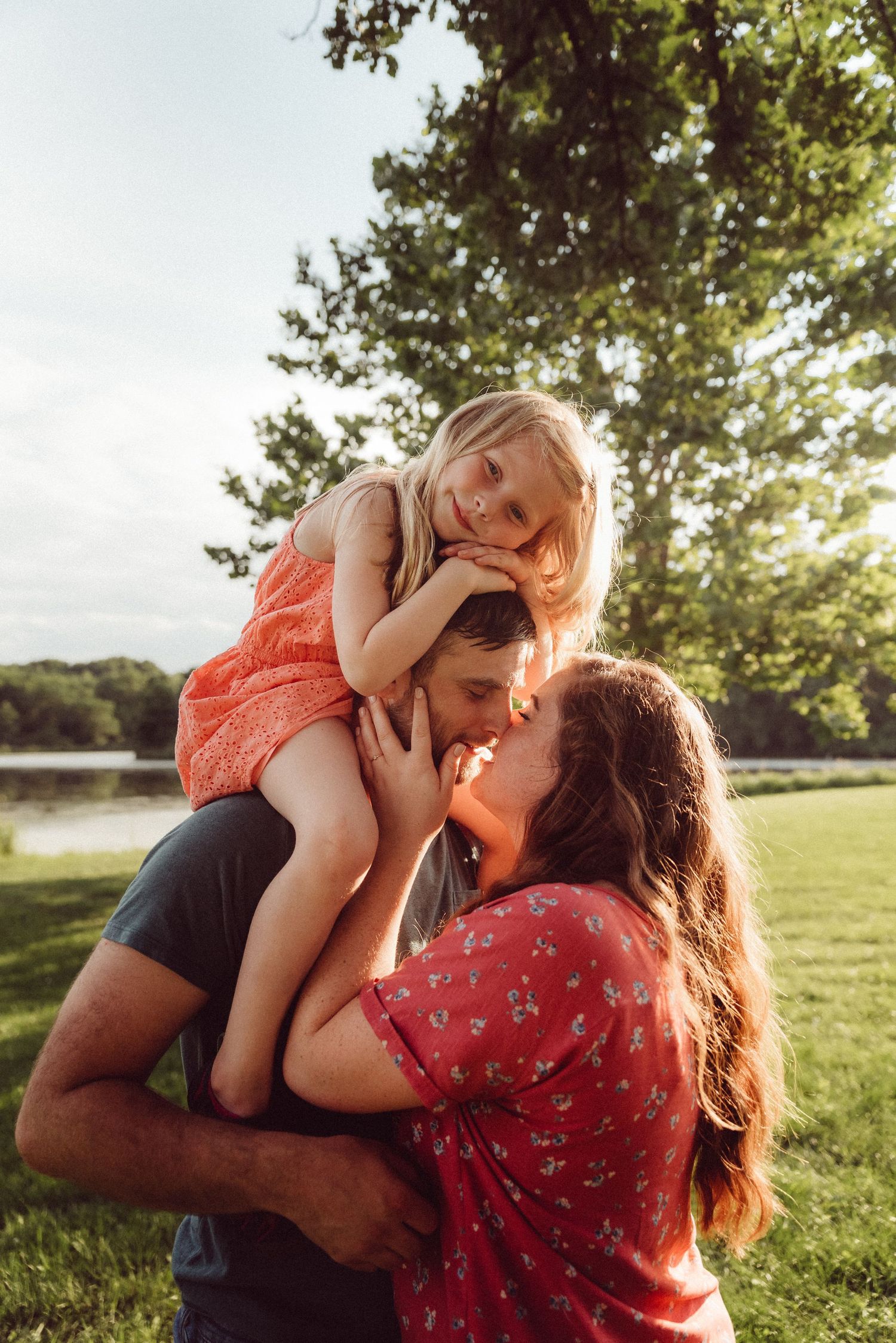 Intimate family moment captured in golden sunlight with joyful expressions and casual outdoor setting.