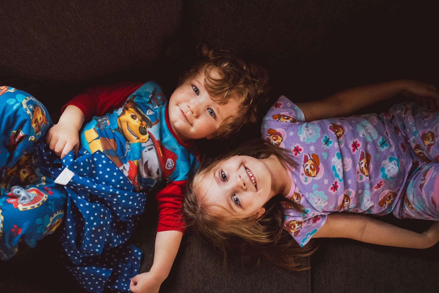 Two children in pajamas lying down and laughing together.