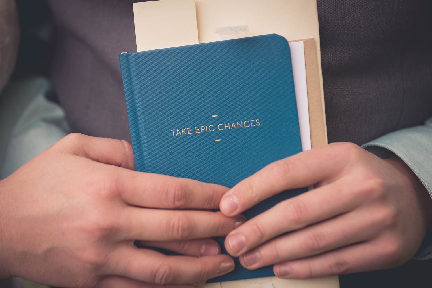 Hands holding a blue notebook with 'Take Epic Chances' text on the cover.