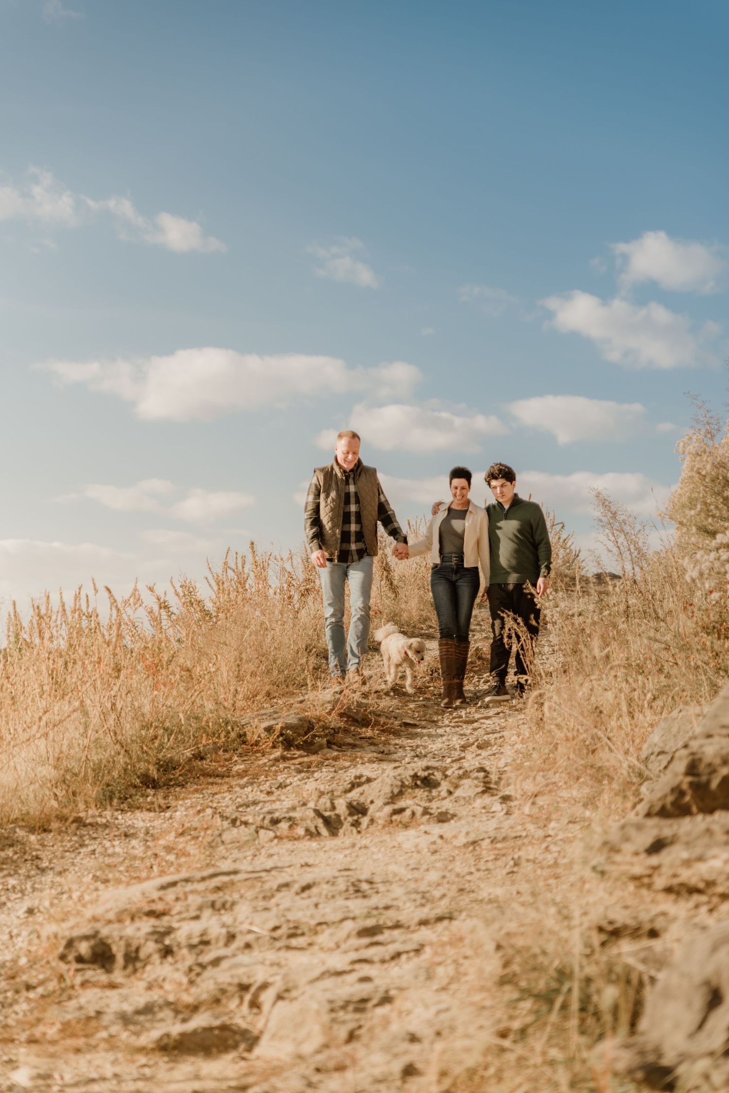 Group walking along hilltop path through dry grass against blue sky backdrop.