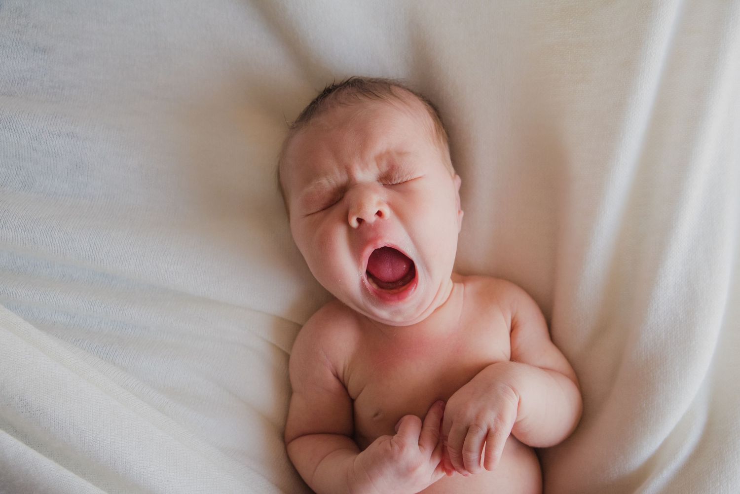 Sleeping newborn baby lying on white bedding in natural light.