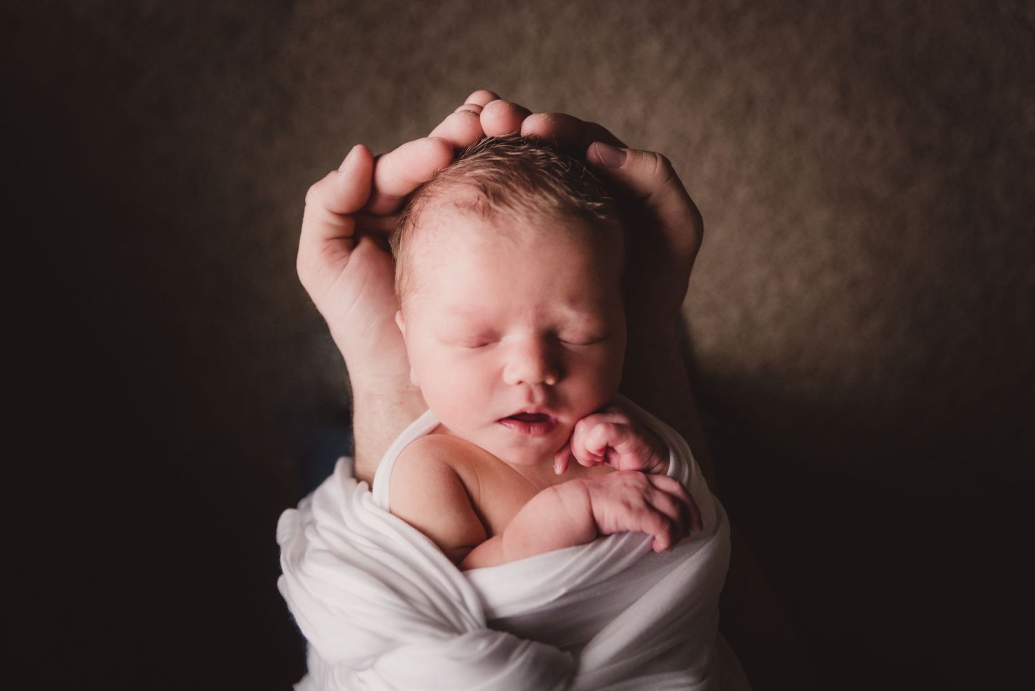 Newborn baby wrapped in white cloth sleeping peacefully during a professional photo shoot.