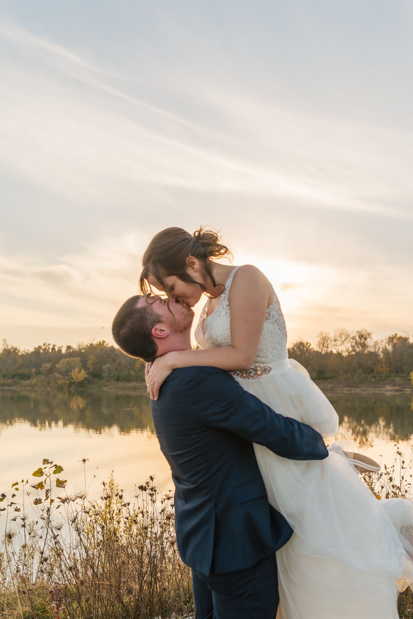 Romantic sunset wedding photos captured by a lake with golden light reflecting on the water.