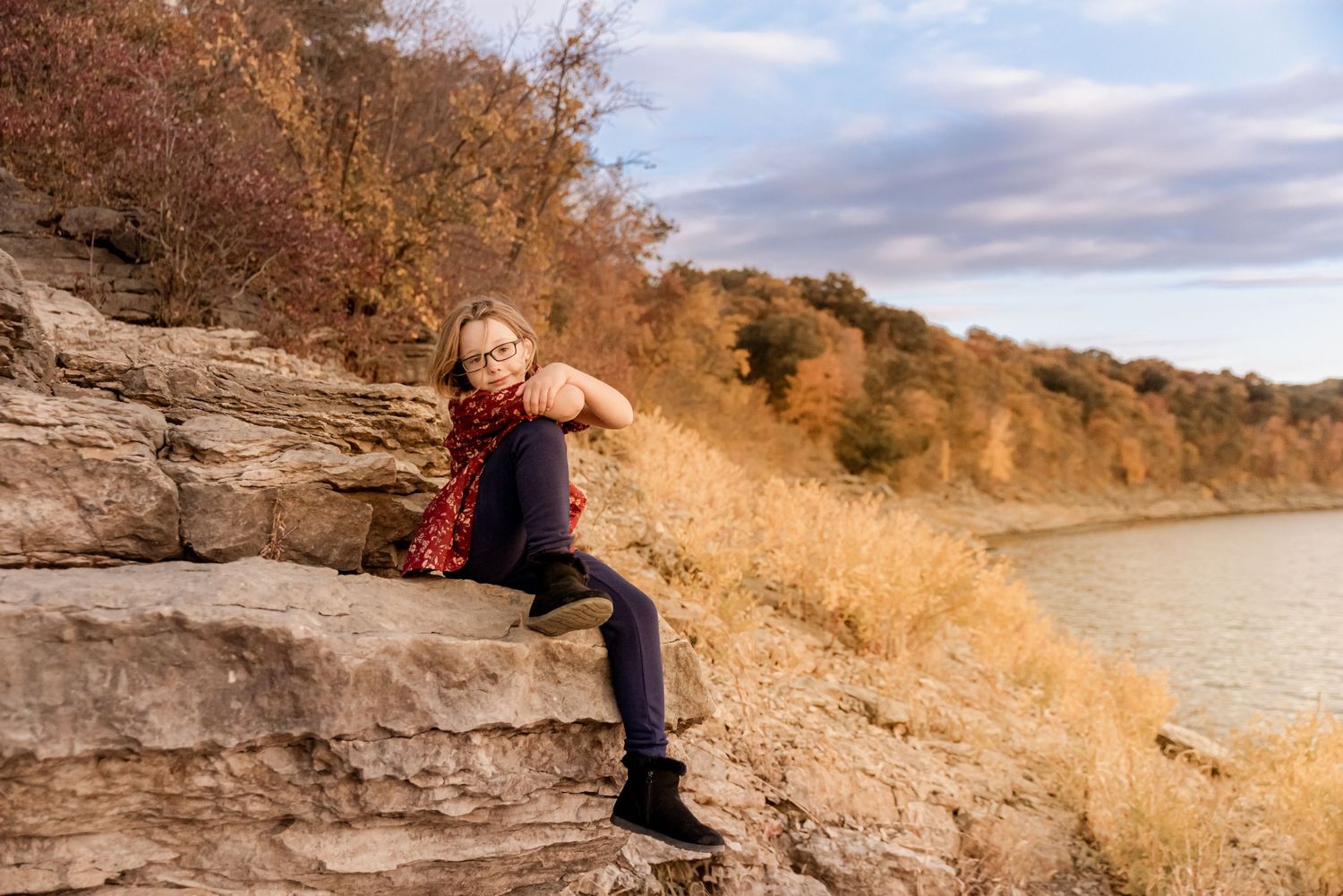 Person sitting on rocky cliff edge overlooking water during golden hour.