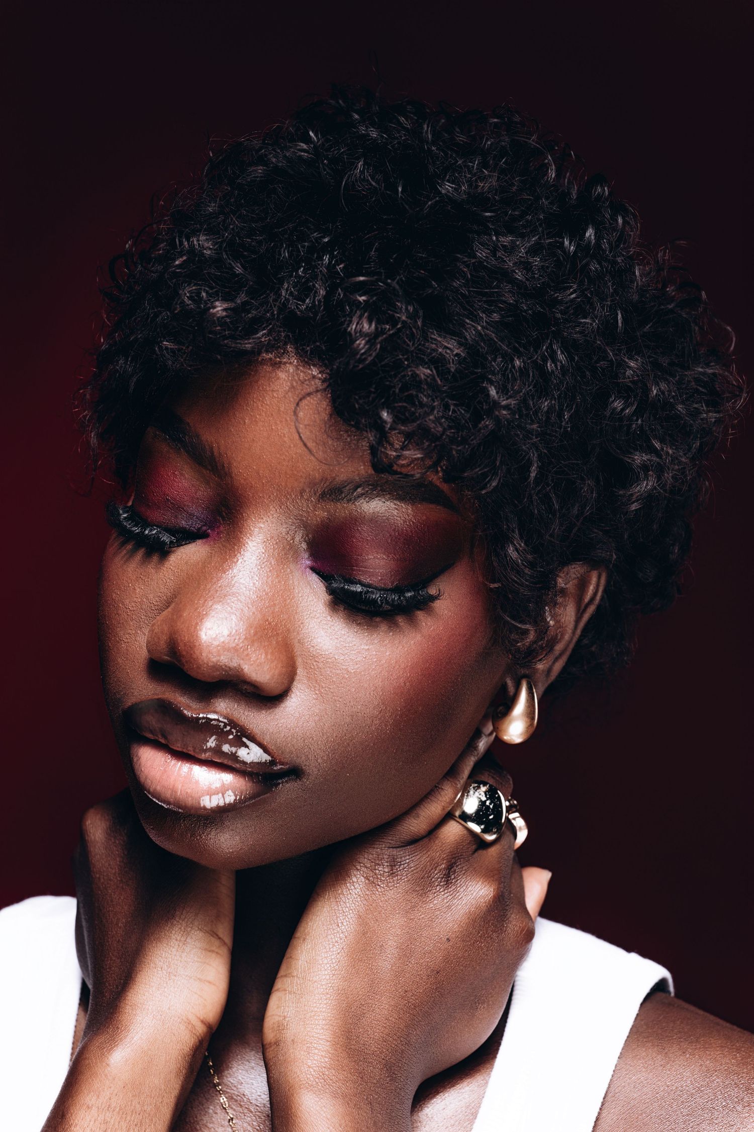 Black lady posing in front of a dark red background with nice makeup and her hands on her neck for a photoshoot in a studio in winnipeg.