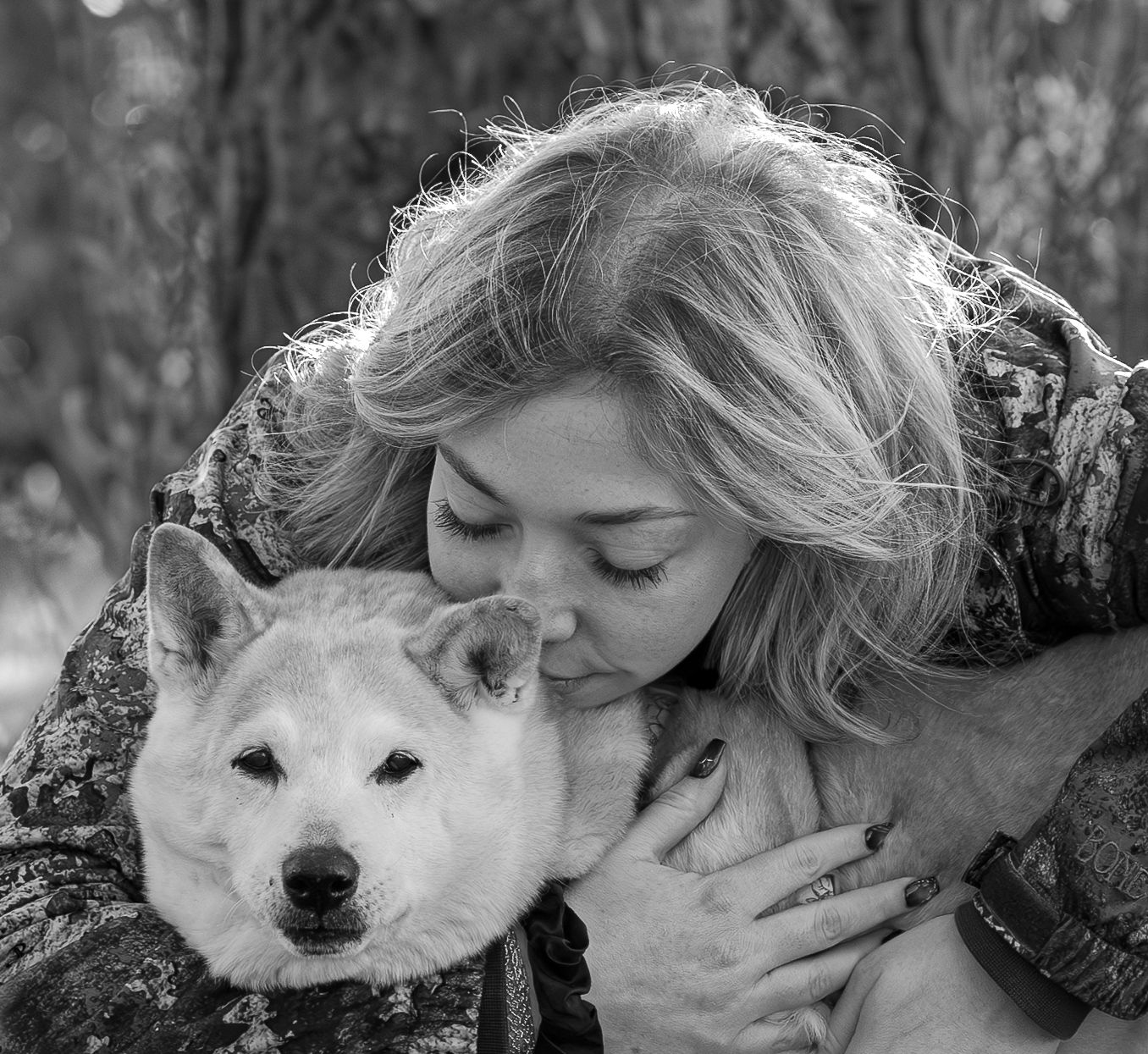 Woman with blonde hair embracing a white Akita dog outdoors in a black and white portrait photo.