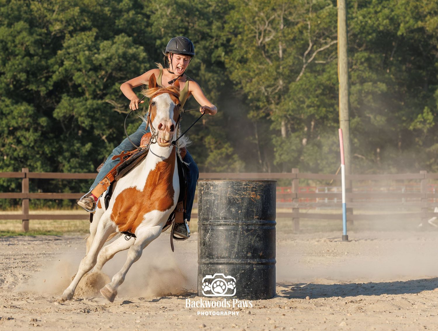 Young rider on a paint horse racing around a barrel in a dusty arena during a barrel racing competition.