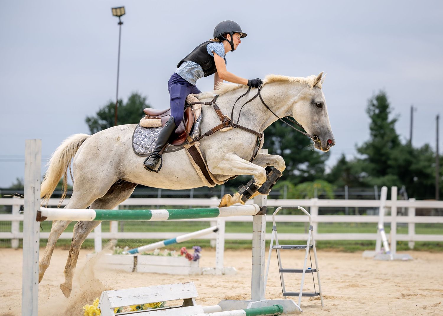 Young rider on palomino horse jumping over hurdle in equestrian show jumping competition on sandy arena.