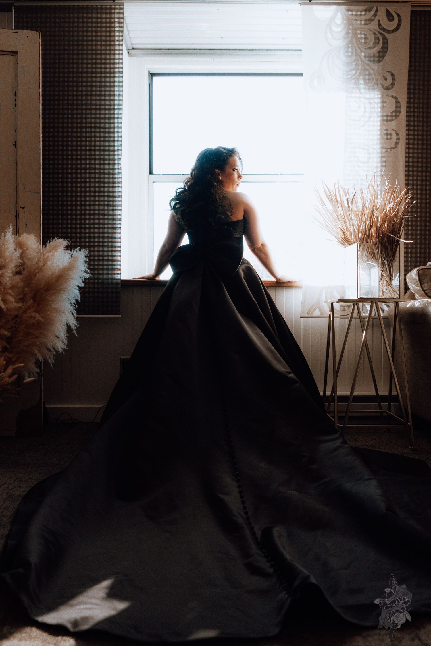 A bride stands in front of a bay window wearing a dazzling black wedding gown by Porsche Aremia