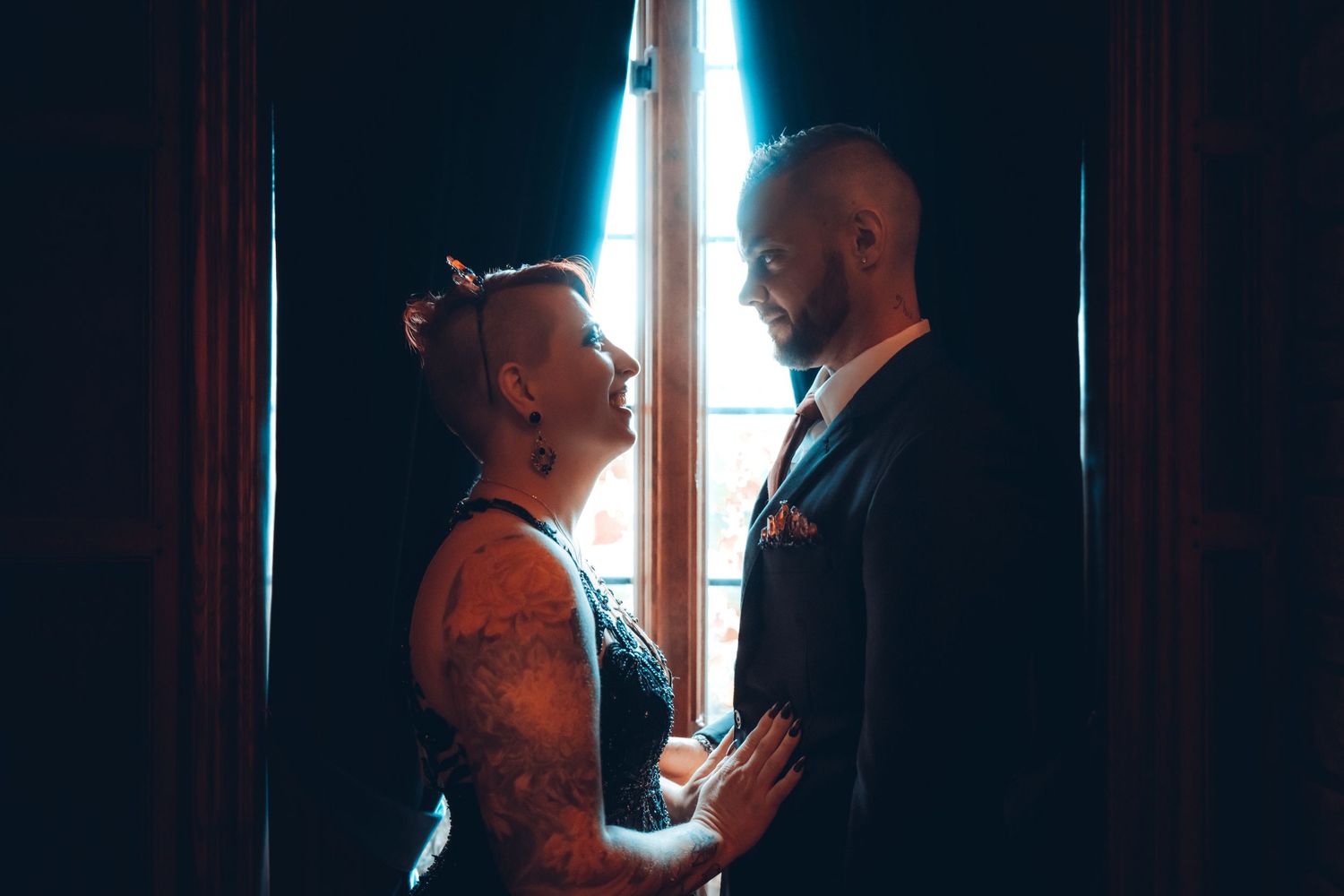 A wedding couple in front of a bay window with dramatic silhouette lighting by Porsche Aremia