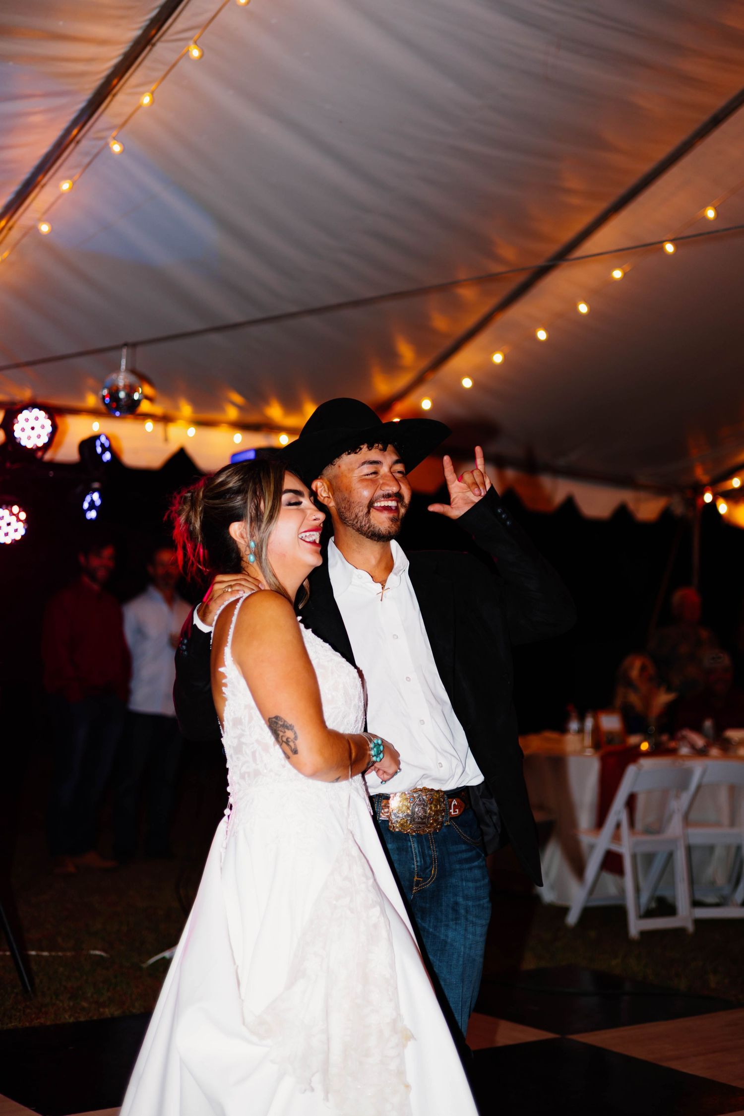 Bride and groom share first dance under string lights in a tent at their rustic country wedding reception.