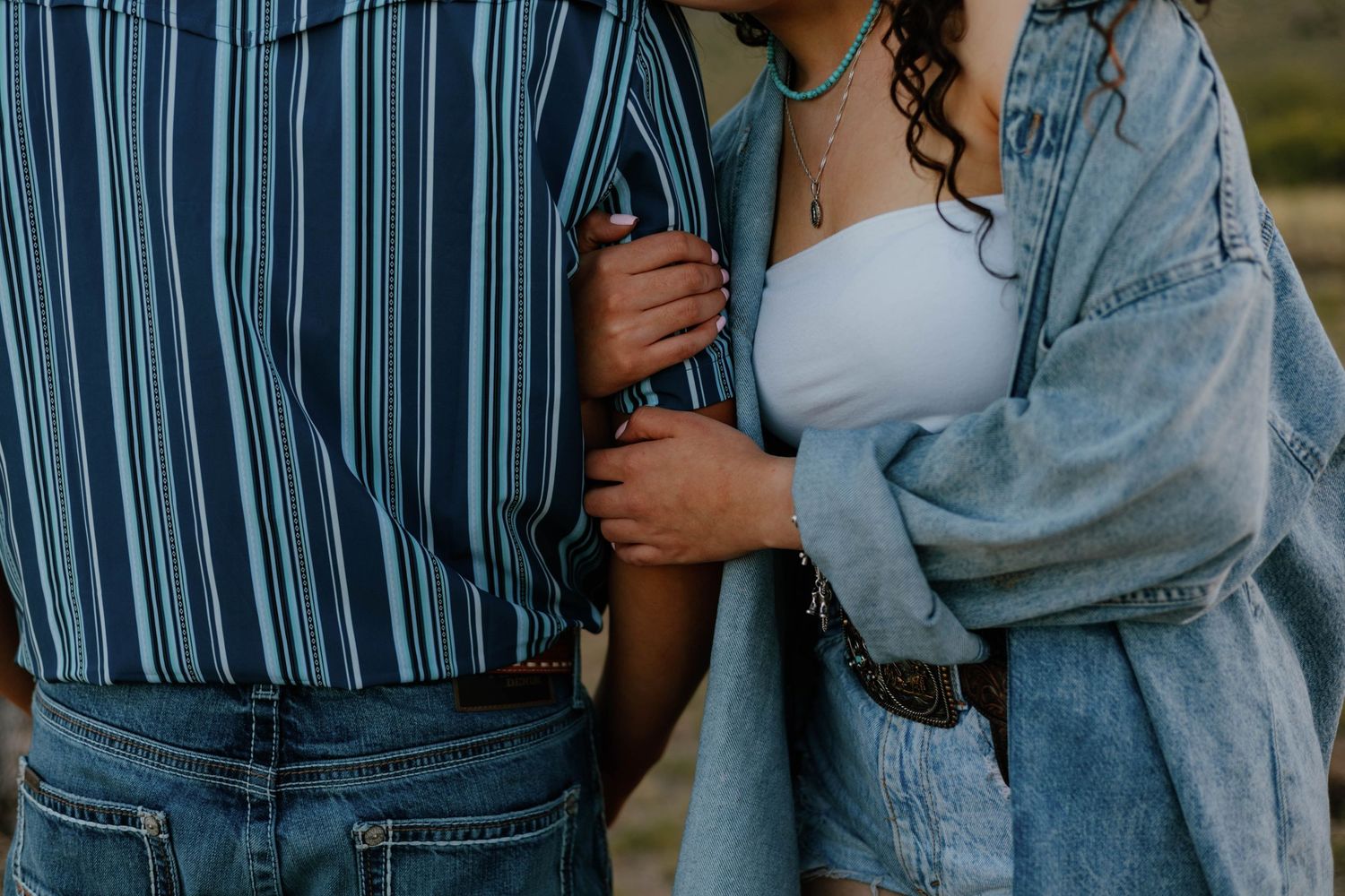 Close-up of couple holding hands, woman in white crop top and denim jacket with man in striped shirt.