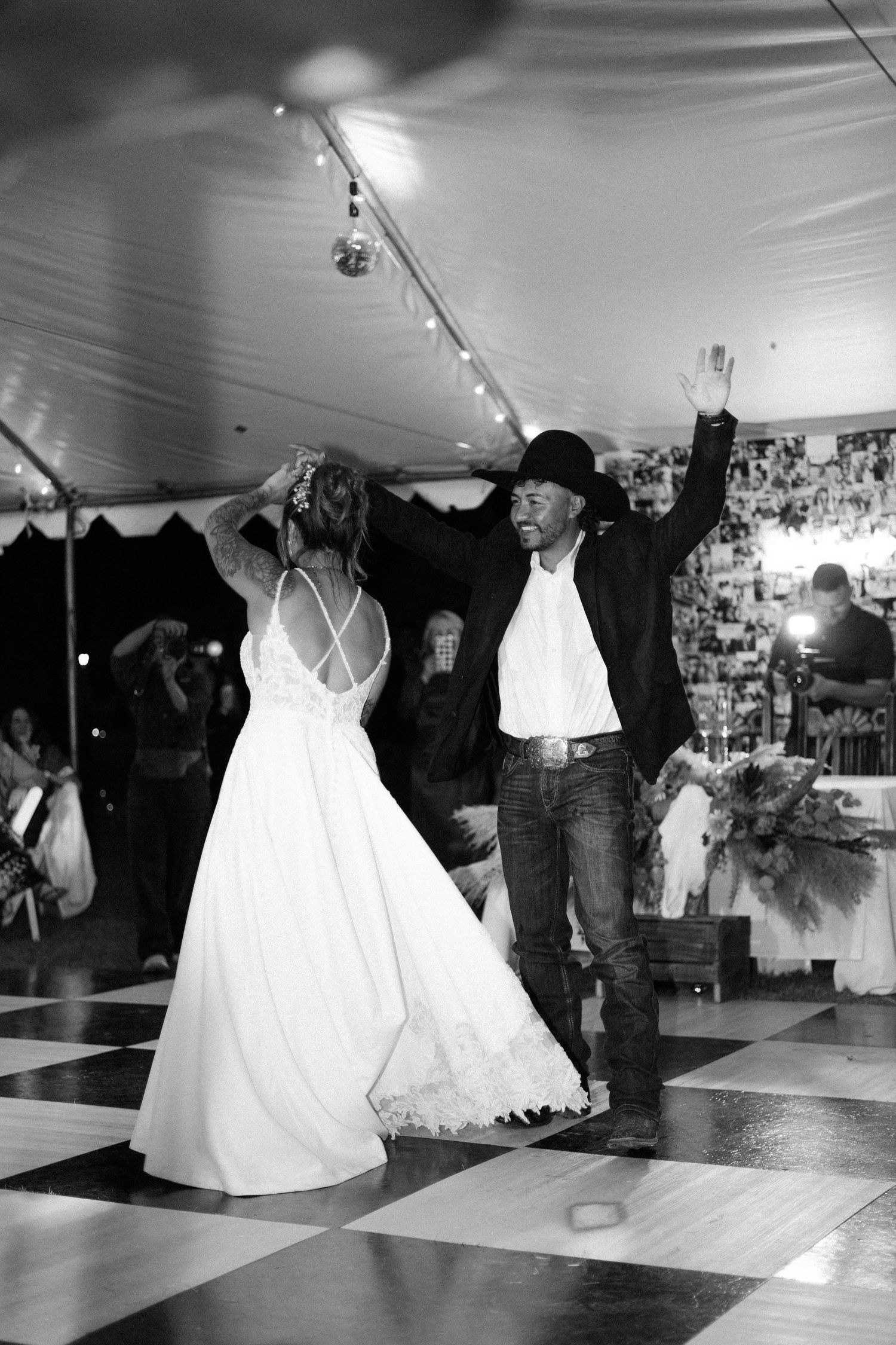 Black and white photo of bride and groom sharing first dance under tent at wedding reception.
