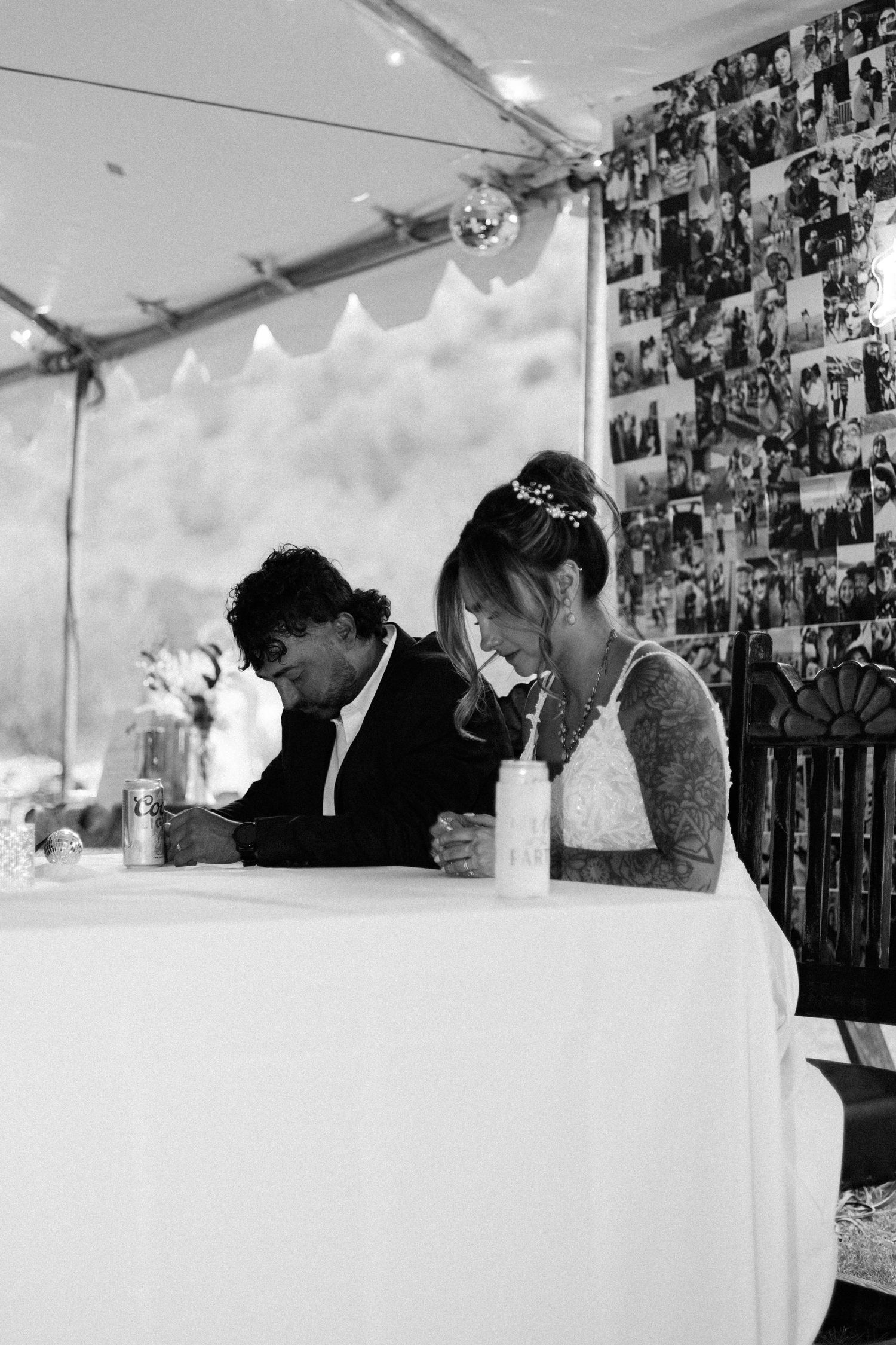 Black and white photo of a bride and groom sitting together at a sweetheart table during their wedding reception.