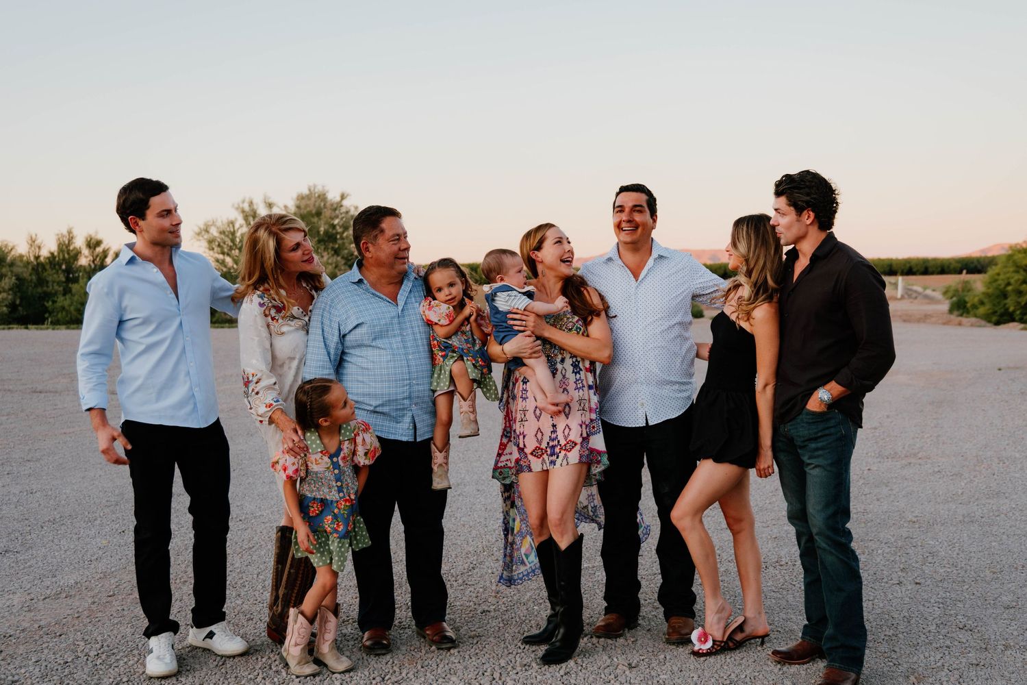 Joyful extended family laughing and embracing during golden hour outdoor photo session in open field.