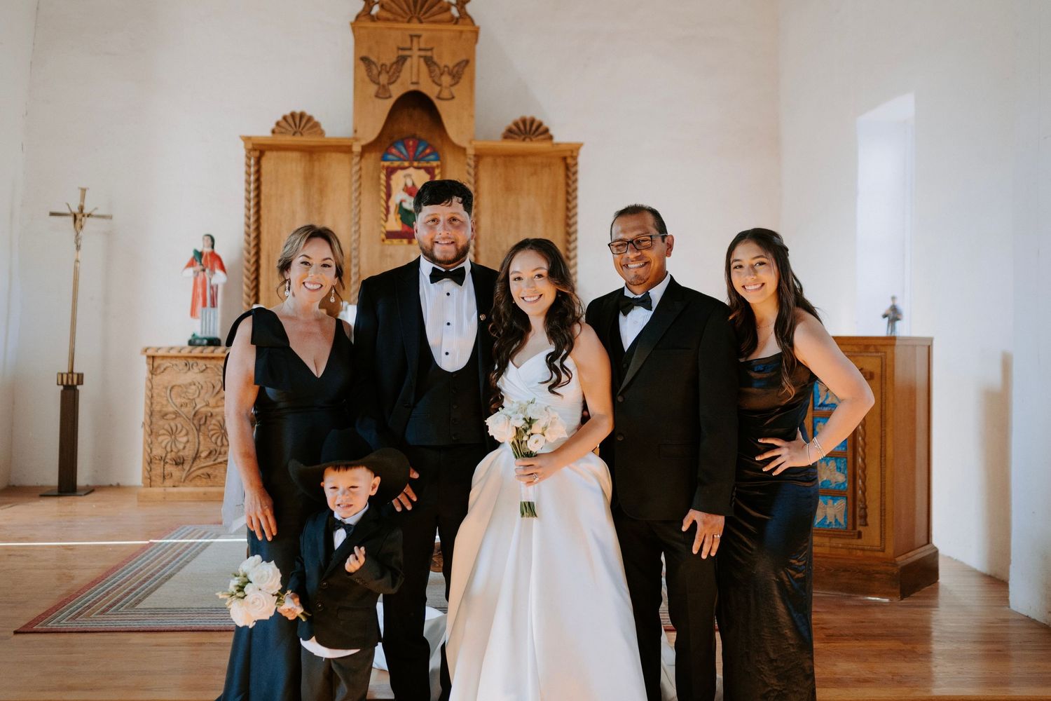 Wedding party of six posing together inside a rustic church with a decorative wooden altar.