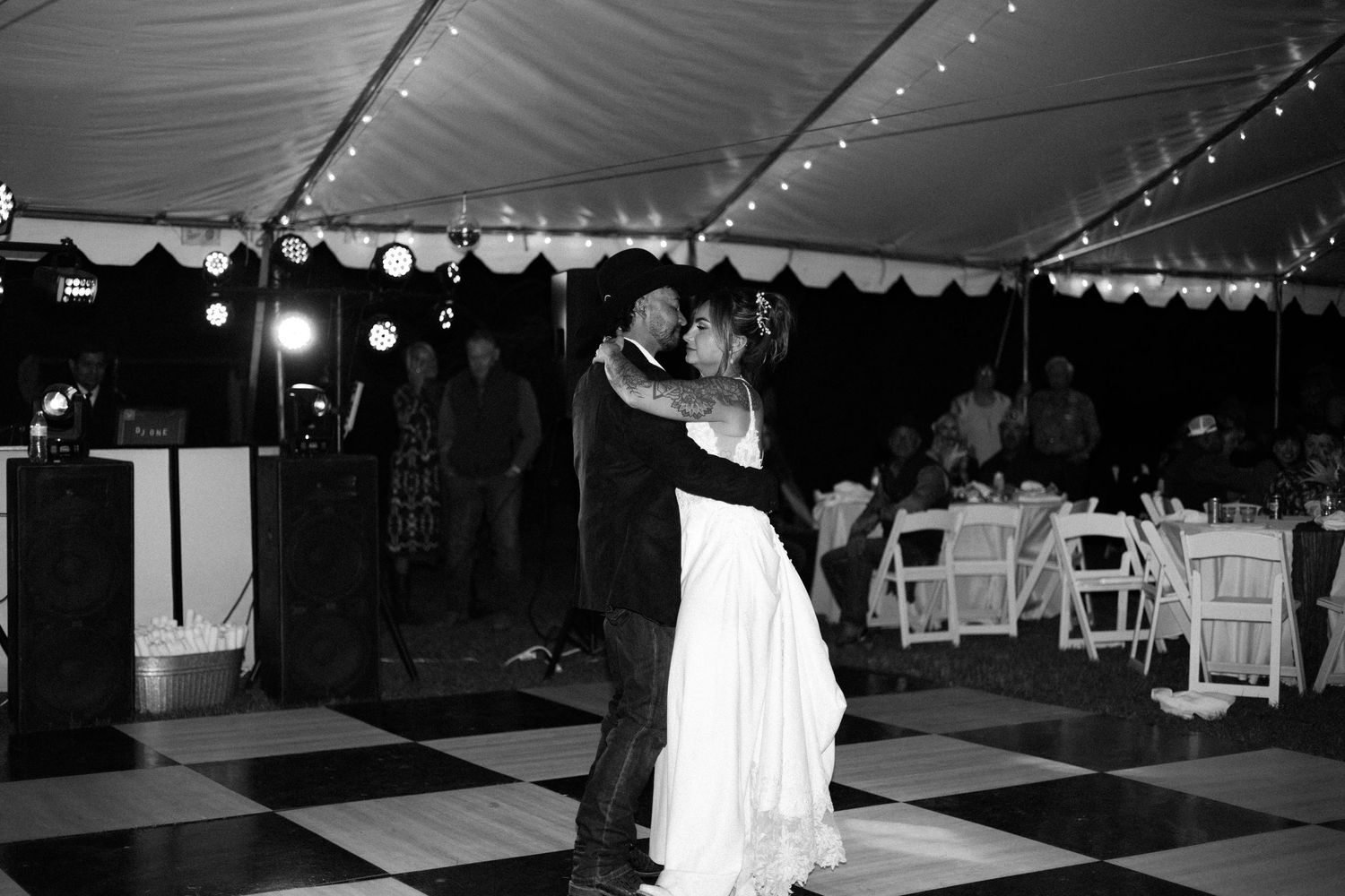 Black and white photo of a couple sharing their first dance under a tent at their wedding reception.