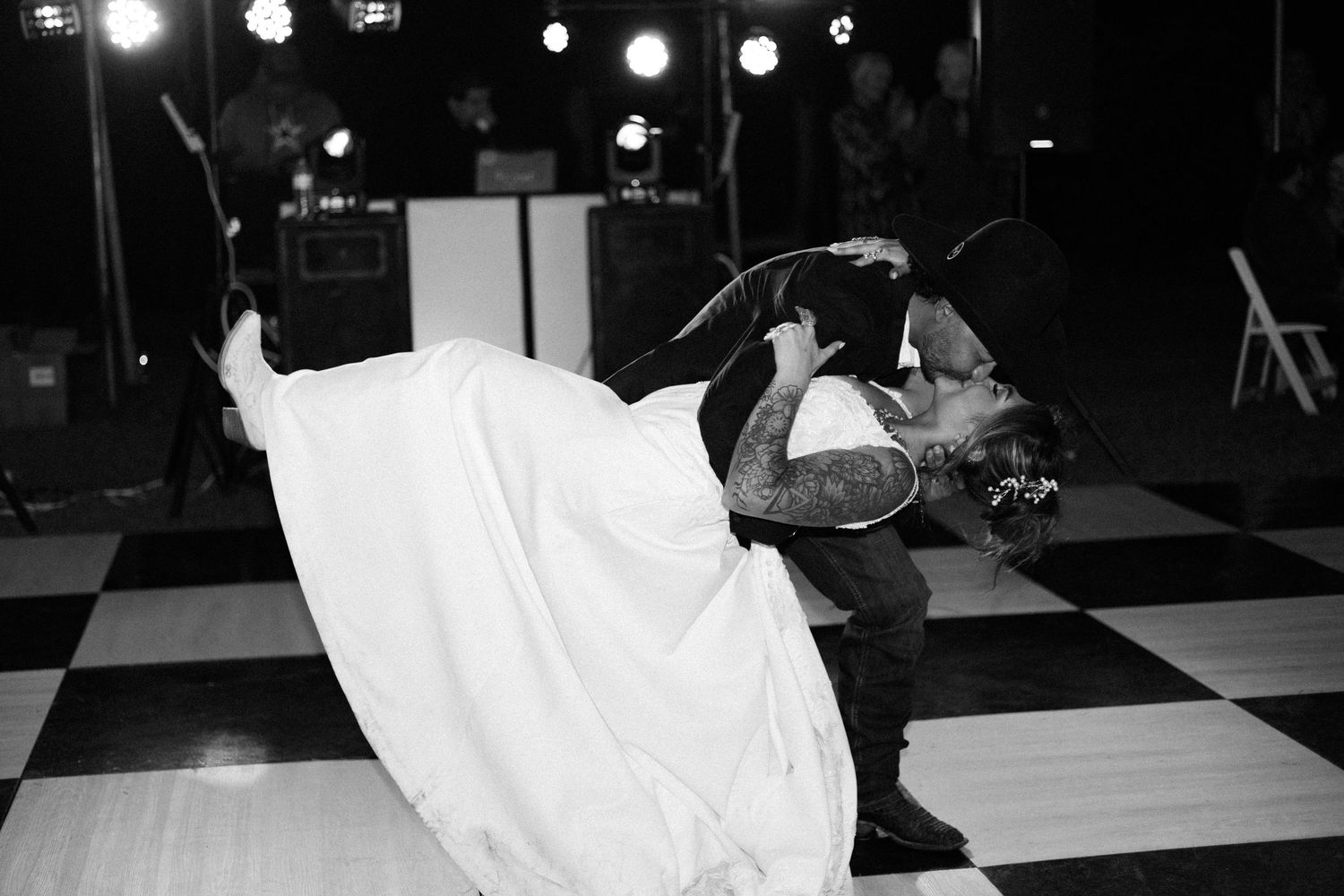 Black and white photo of groom dipping bride during romantic first dance on checkered dance floor at wedding reception.