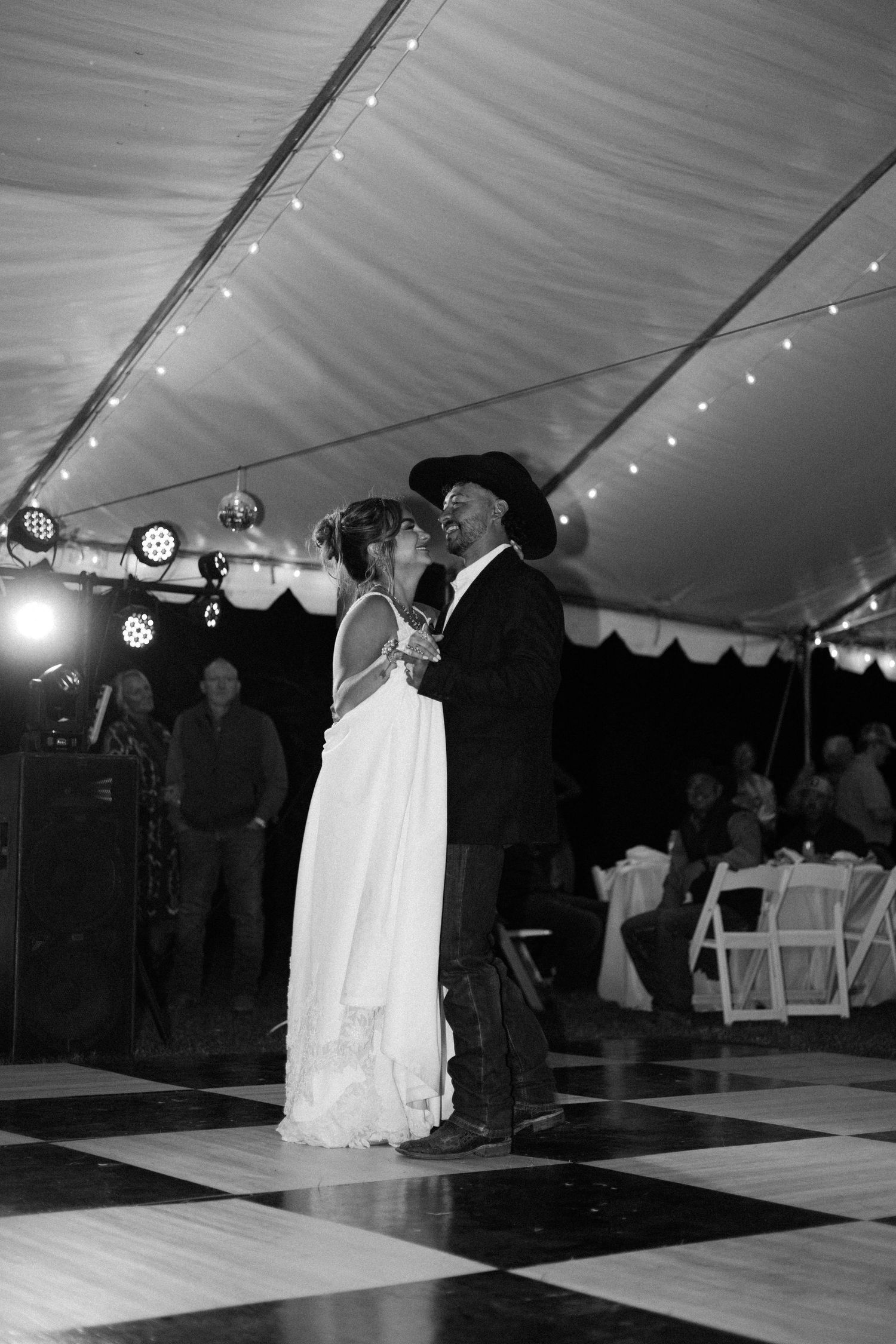 Bride and groom share first dance under a tent with string lights at a country wedding reception.