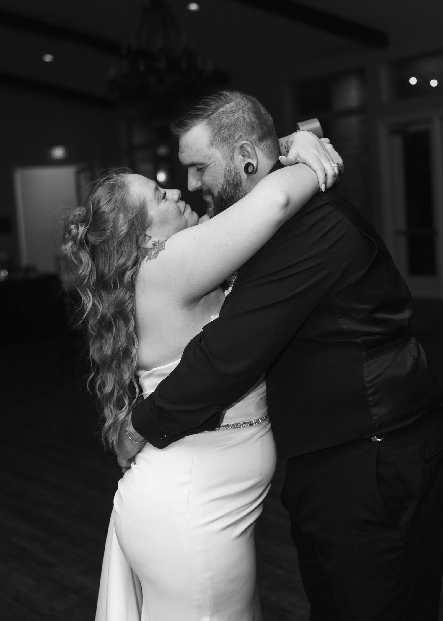 Black and white photo of a couple sharing their first dance, embracing closely in wedding attire.