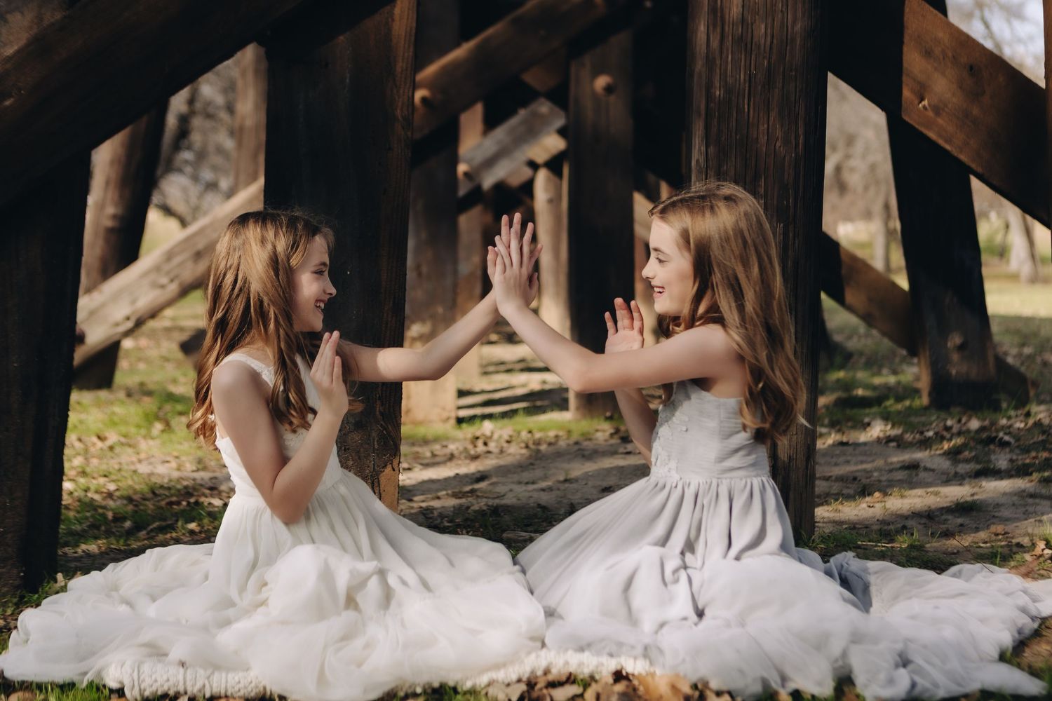 Two dancers in white dresses performing outdoors under wooden beams.