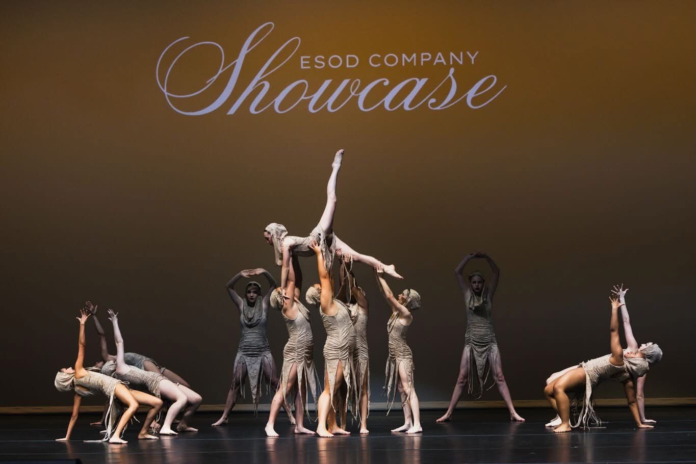 Dance performers in neutral costumes create dynamic formations during a showcase performance on stage.